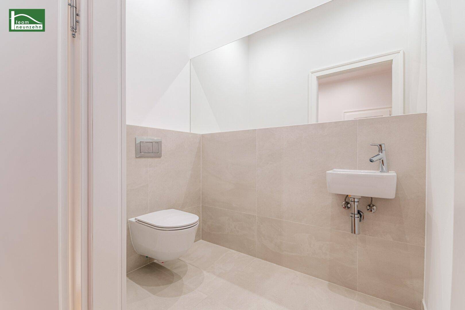 Elegantes Gäste-WC mit wandhängender Toilette, kleinem Waschbecken und großem Spiegel.
