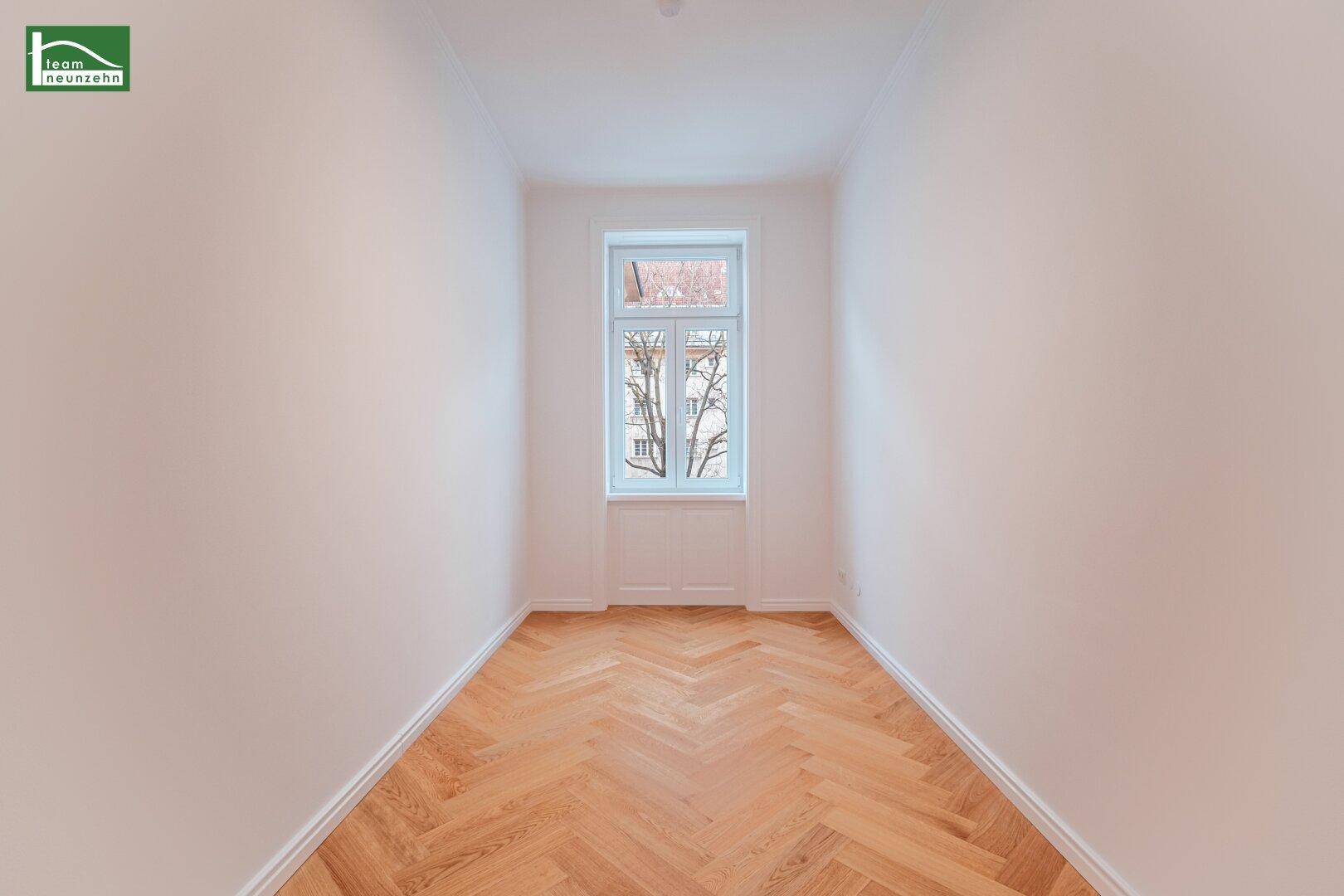 Schmaler, heller Raum mit einem Fenster und klassischem Fischgrätparkett, ideal als Schlafzimmer.