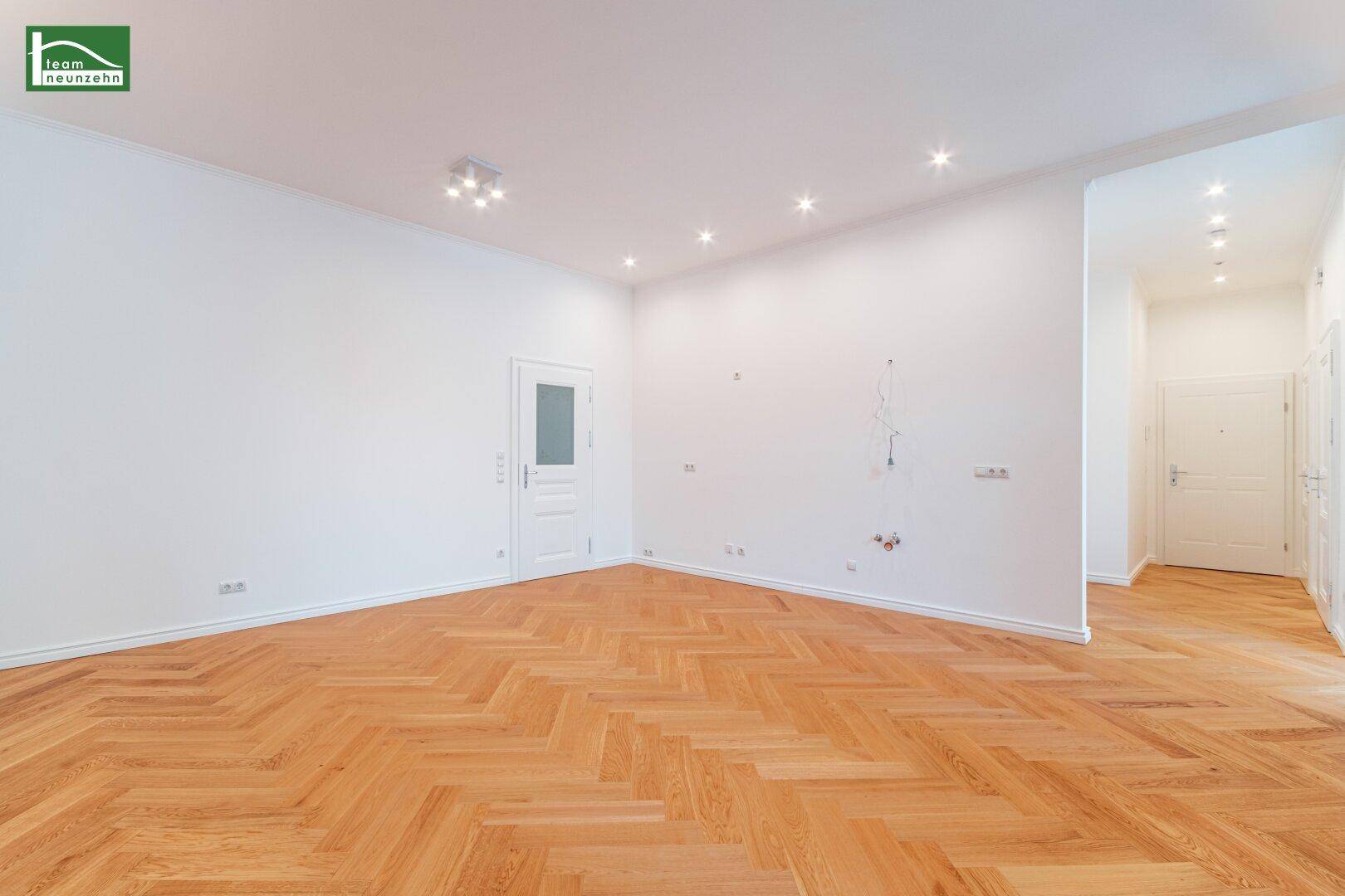 Großer, heller Wohnbereich mit Fischgrätparkett und moderner Beleuchtung, ideal für geselliges Beisammensein.