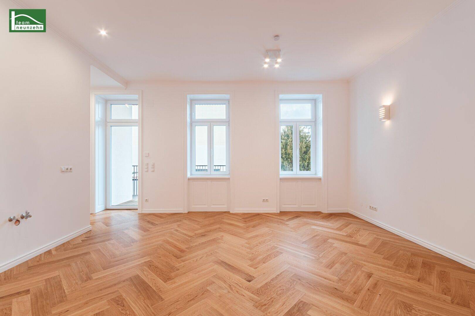 Geräumiges Wohnzimmer mit Fischgrätparkett, Einbaustrahlern und direktem Zugang zum Balkon.