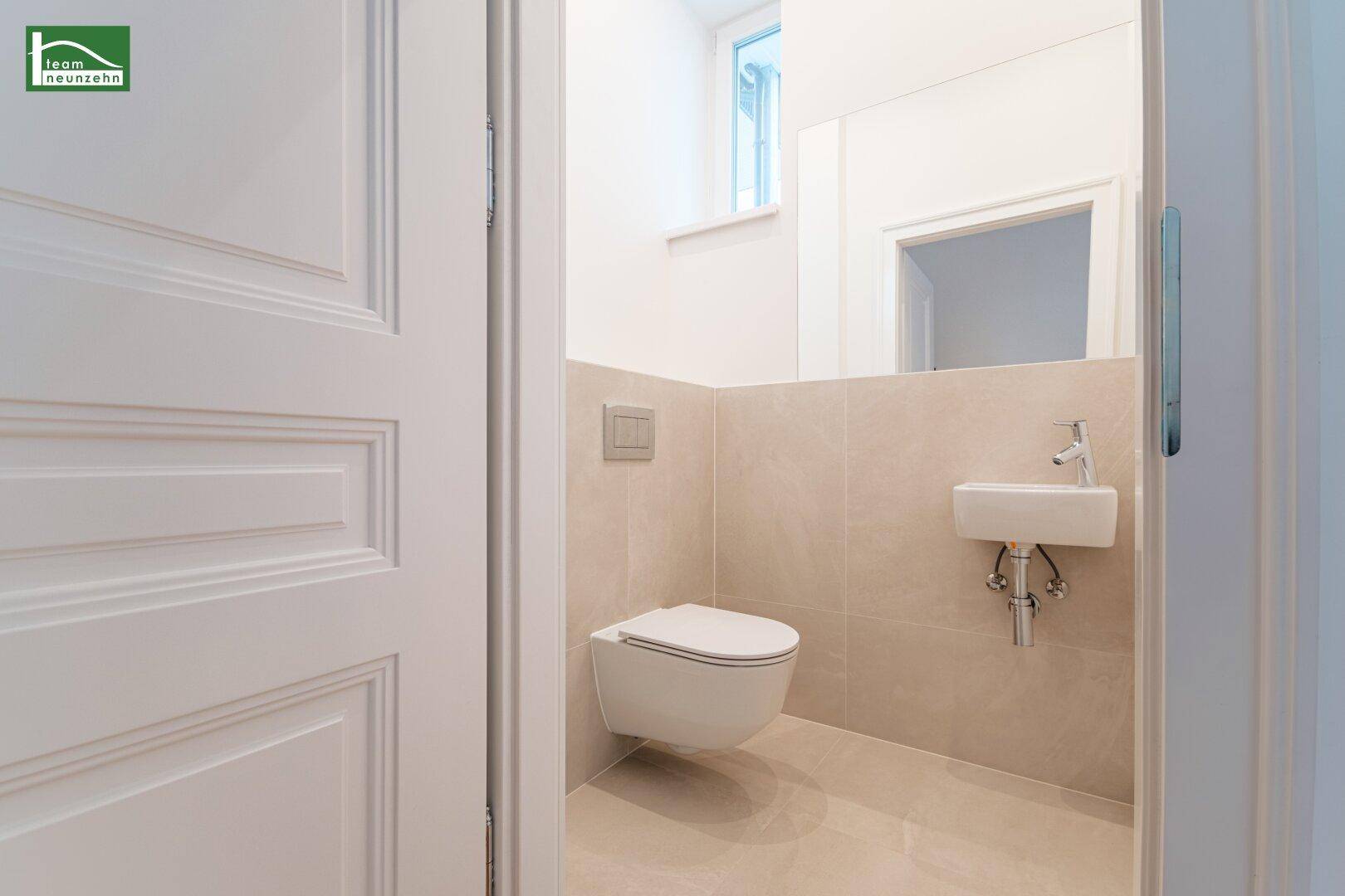 Modernes Gäste-WC mit wandhängender Toilette, kleinem Waschbecken und eleganten Fliesen.