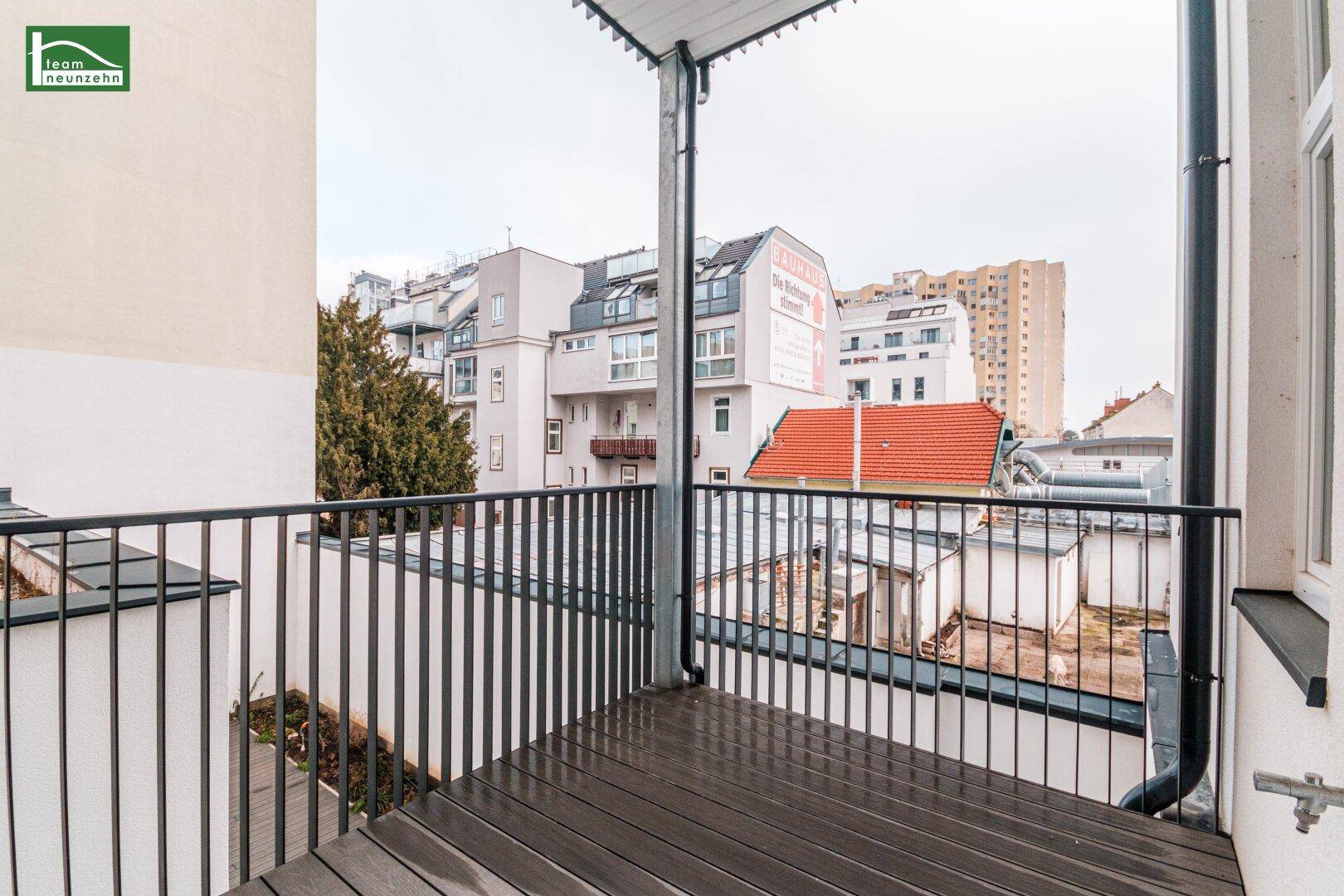 Geräumiger Balkon mit dunklem Geländer und Blick auf die Nachbarschaft und Dächer.