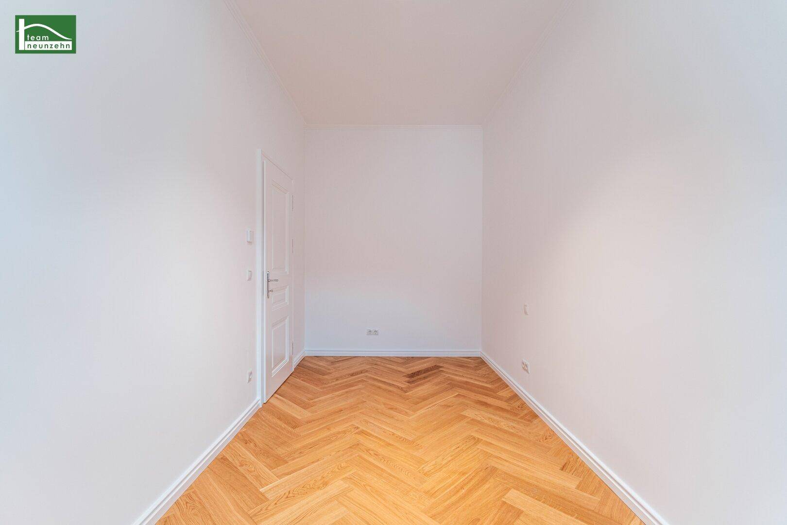 Leeres Zimmer mit hellem Fischgrätparkett und einer weißen Tür, bereit zur individuellen Gestaltung.