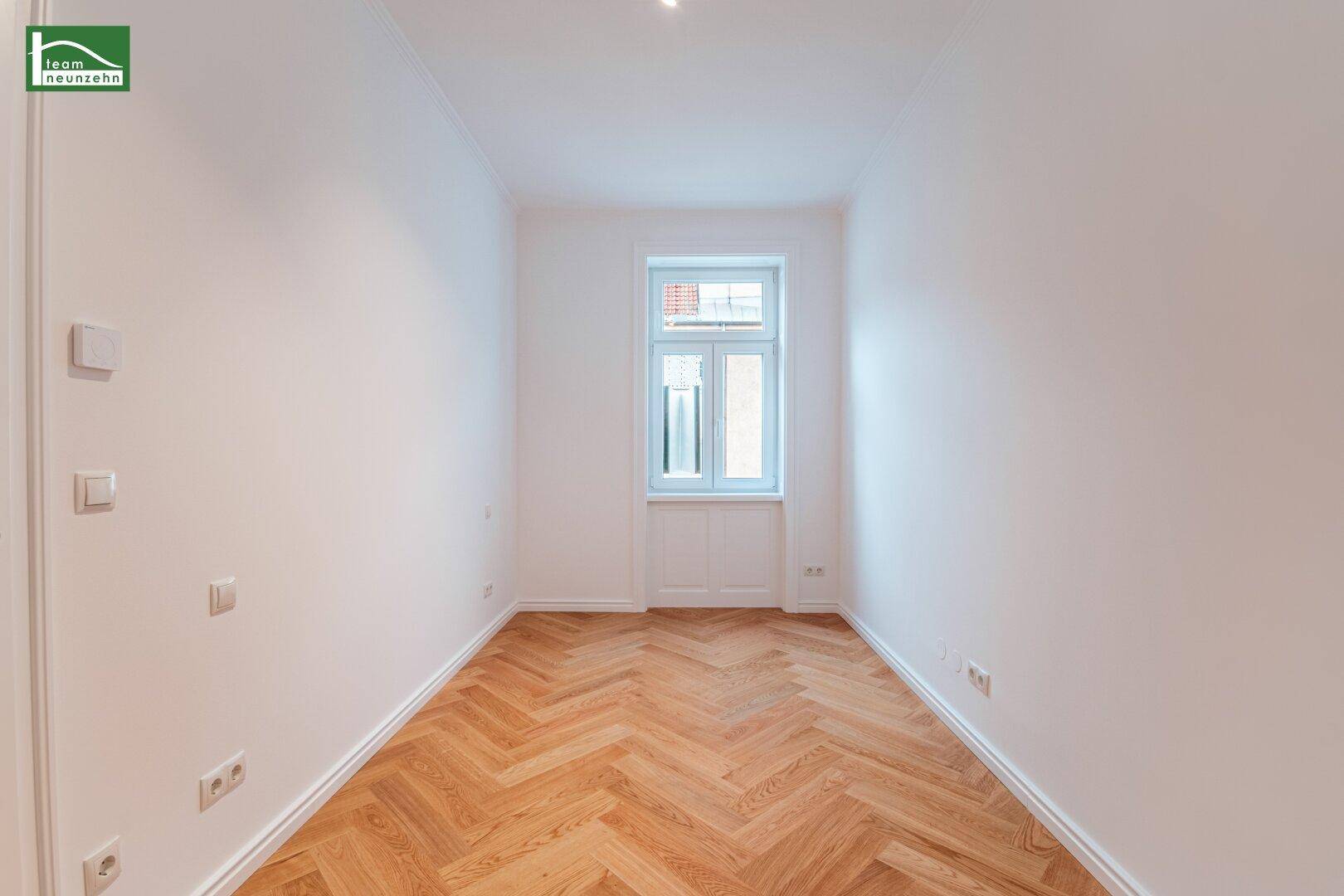 Lichtdurchflutetes Zimmer mit Fischgrätparkett und einem hohen Fenster, ideal für ein Schlafzimmer.