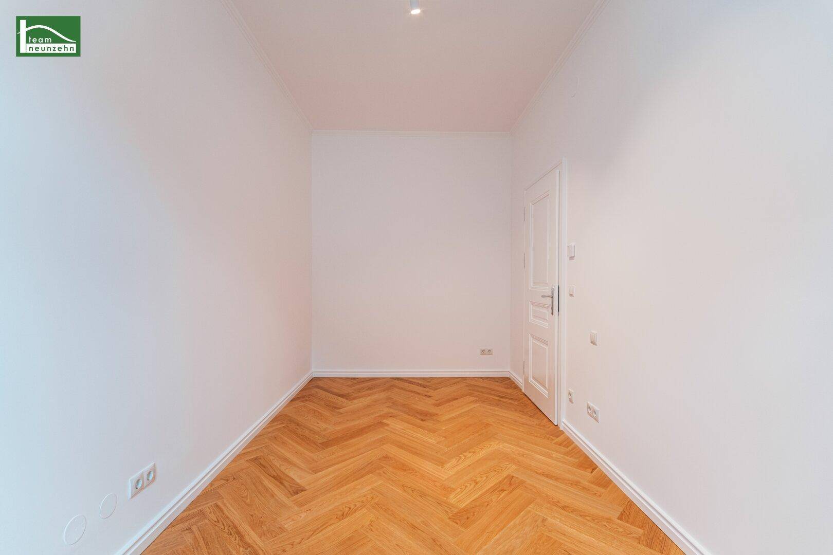 Geräumiges, leeres Zimmer mit Fischgrätparkett und einer weißen Tür, bietet viel Gestaltungspotenzial.