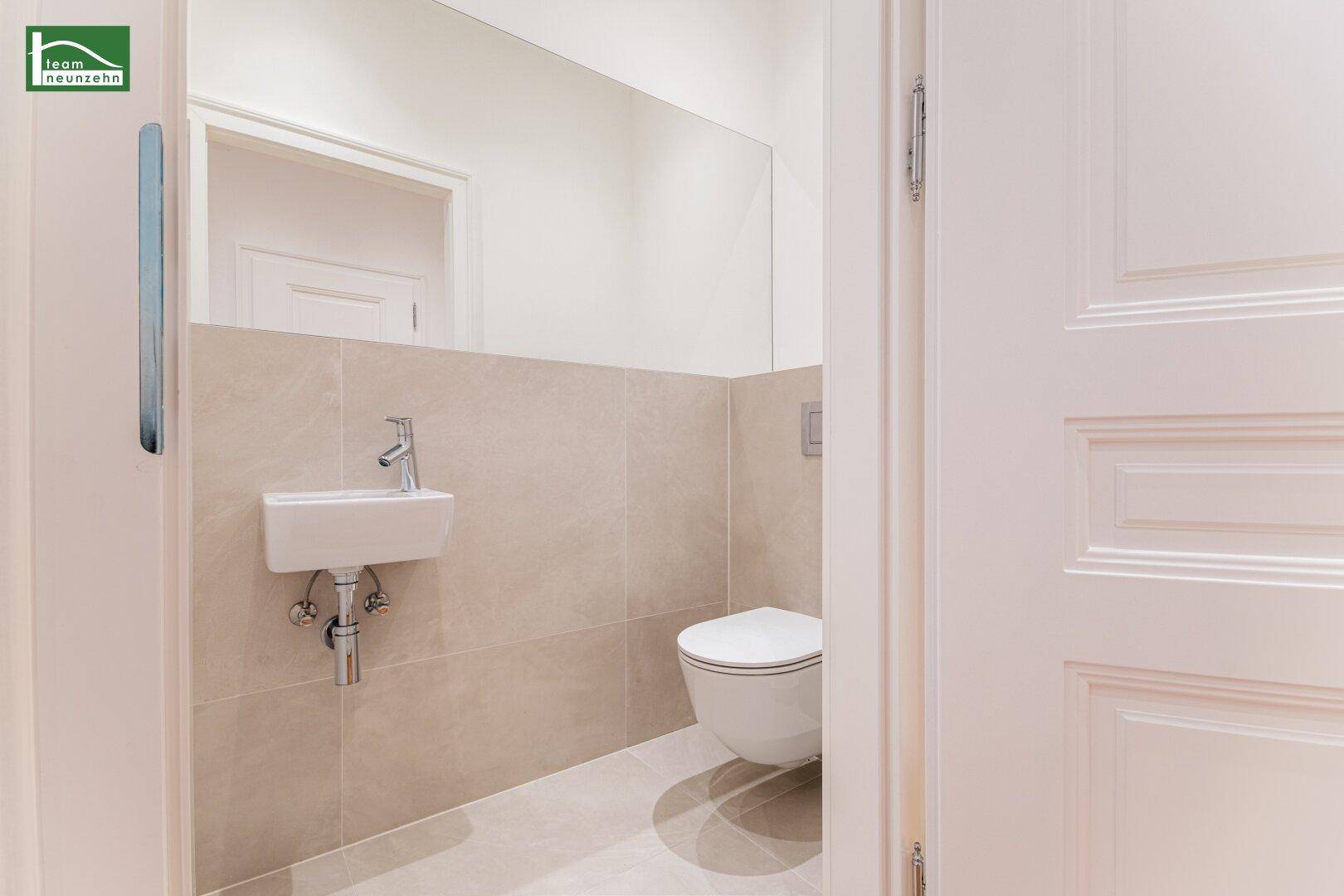 Elegantes Gäste-WC mit wandmontierter Toilette und kleinem Waschbecken, modern gefliest.