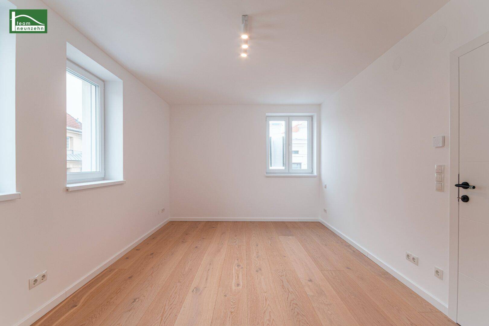 Heller Raum mit Holzboden und weißen Wänden, ausgestattet mit modernen Deckenleuchten und Steckdosen.
