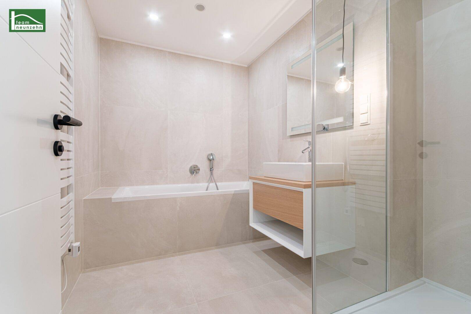 Elegantes Badezimmer mit Badewanne, separater Dusche und modernem Waschtisch mit Holzdetails.