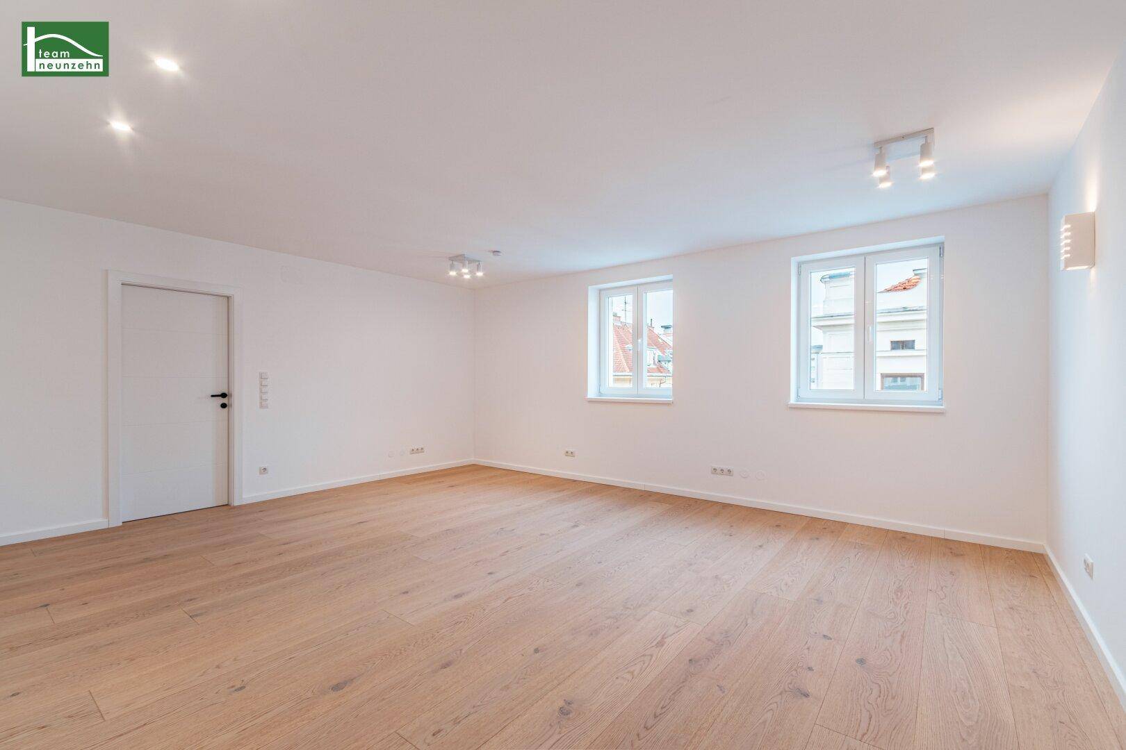 Weitläufiger, heller Raum mit Holzboden und mehreren Fenstern, ausgestattet mit Deckenleuchten.