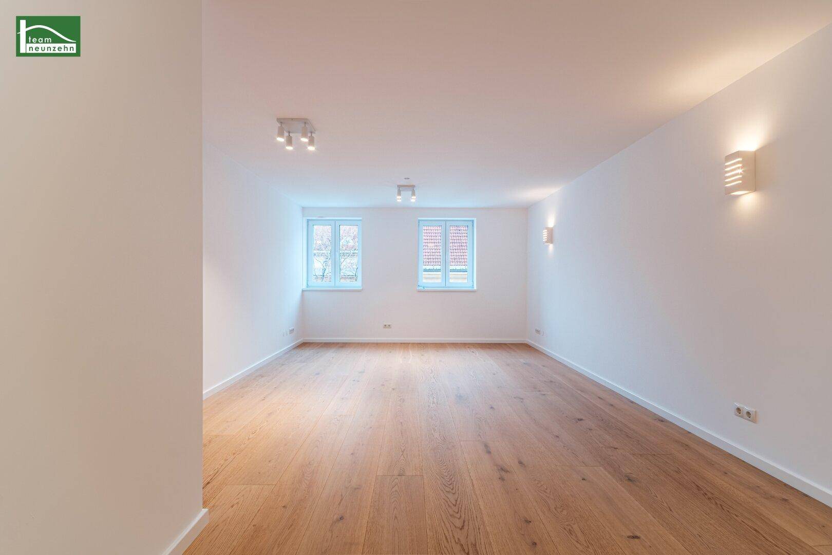 Helles, leeres Zimmer mit Holzboden und zwei Fenstern, bereit zur individuellen Gestaltung.