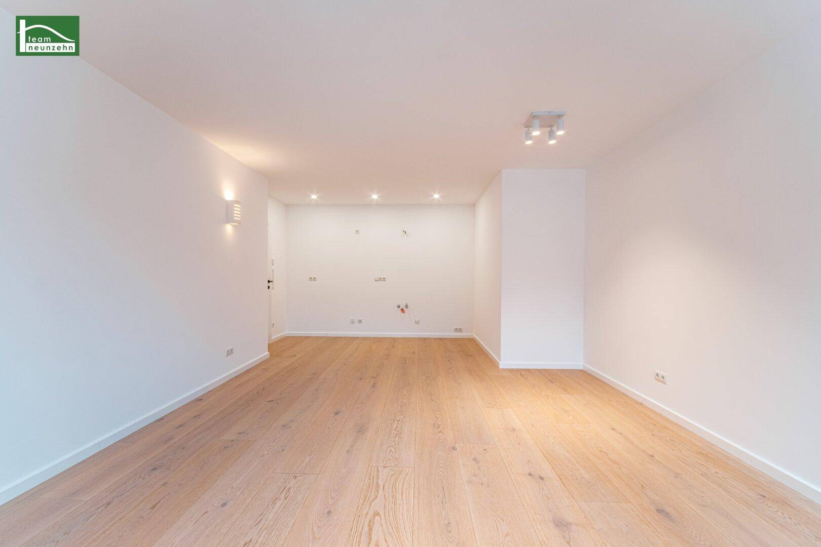 Großzügiger, heller Wohnbereich mit Holzboden und moderner Deckenbeleuchtung.