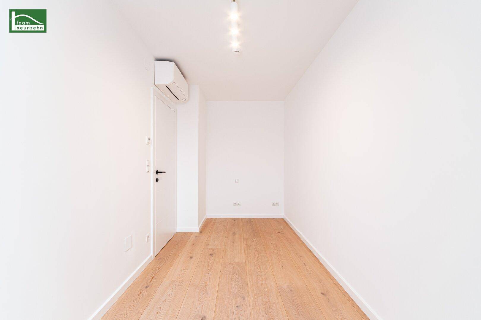 Helles Zimmer mit Holzboden, Klimaanlage und moderner Beleuchtung.