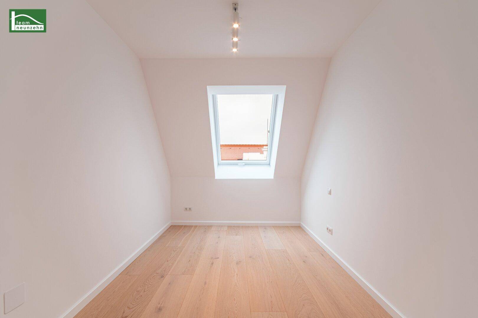 Leeres Zimmer im Dachgeschoss mit hellem Holzboden und einem Dachfenster.