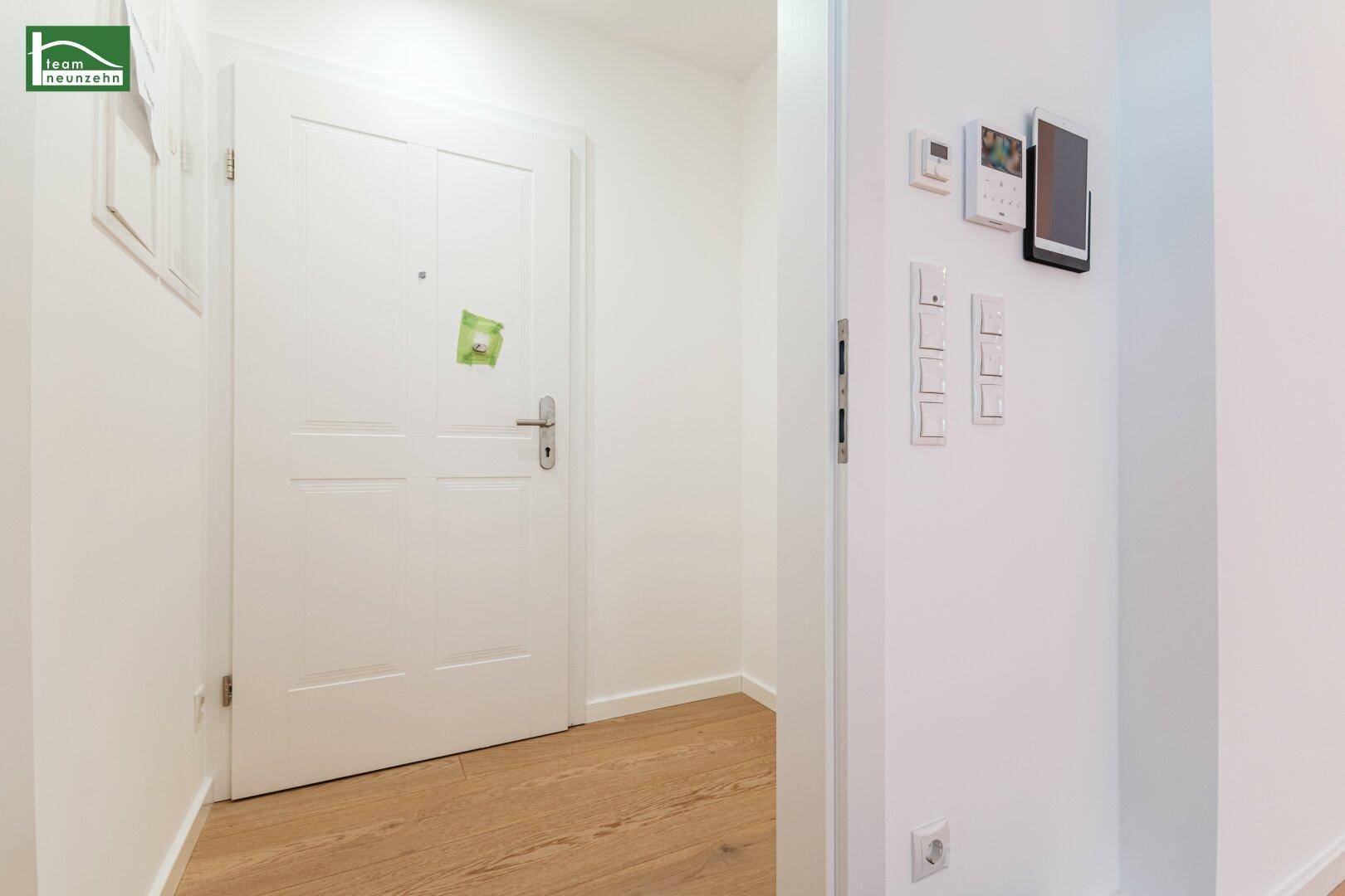 Eingangsbereich mit moderner Tür und Steuerungselementen an der Wand.
