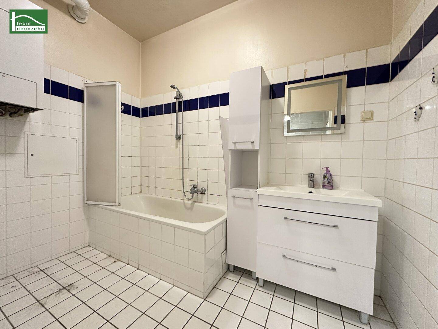 Badezimmer mit Badewanne, Waschbecken und weißen Fliesen, akzentuiert durch blaue Streifen.