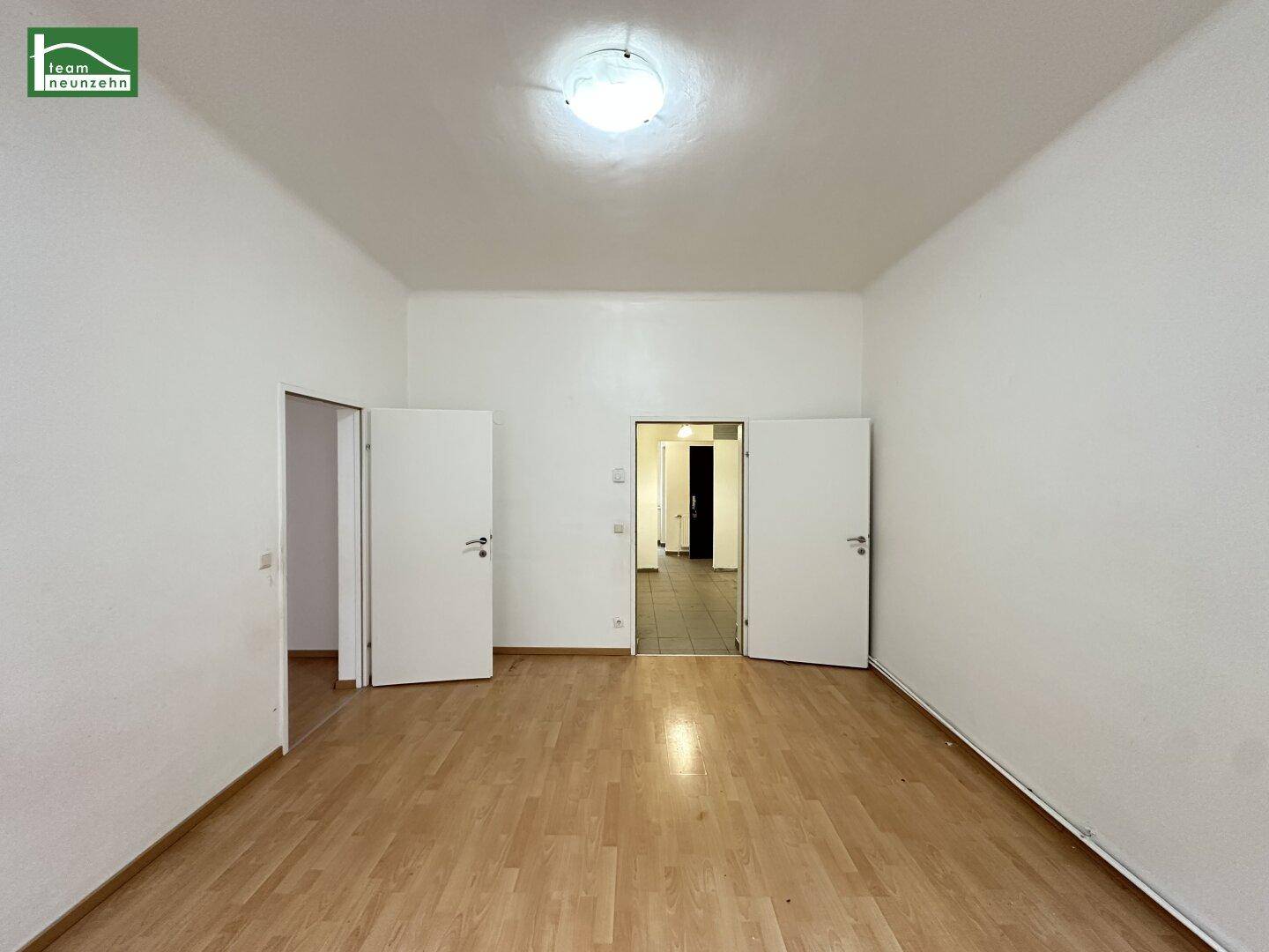 Geräumiger, heller Raum mit Holzparkett und Zugang zu weiteren Zimmern.