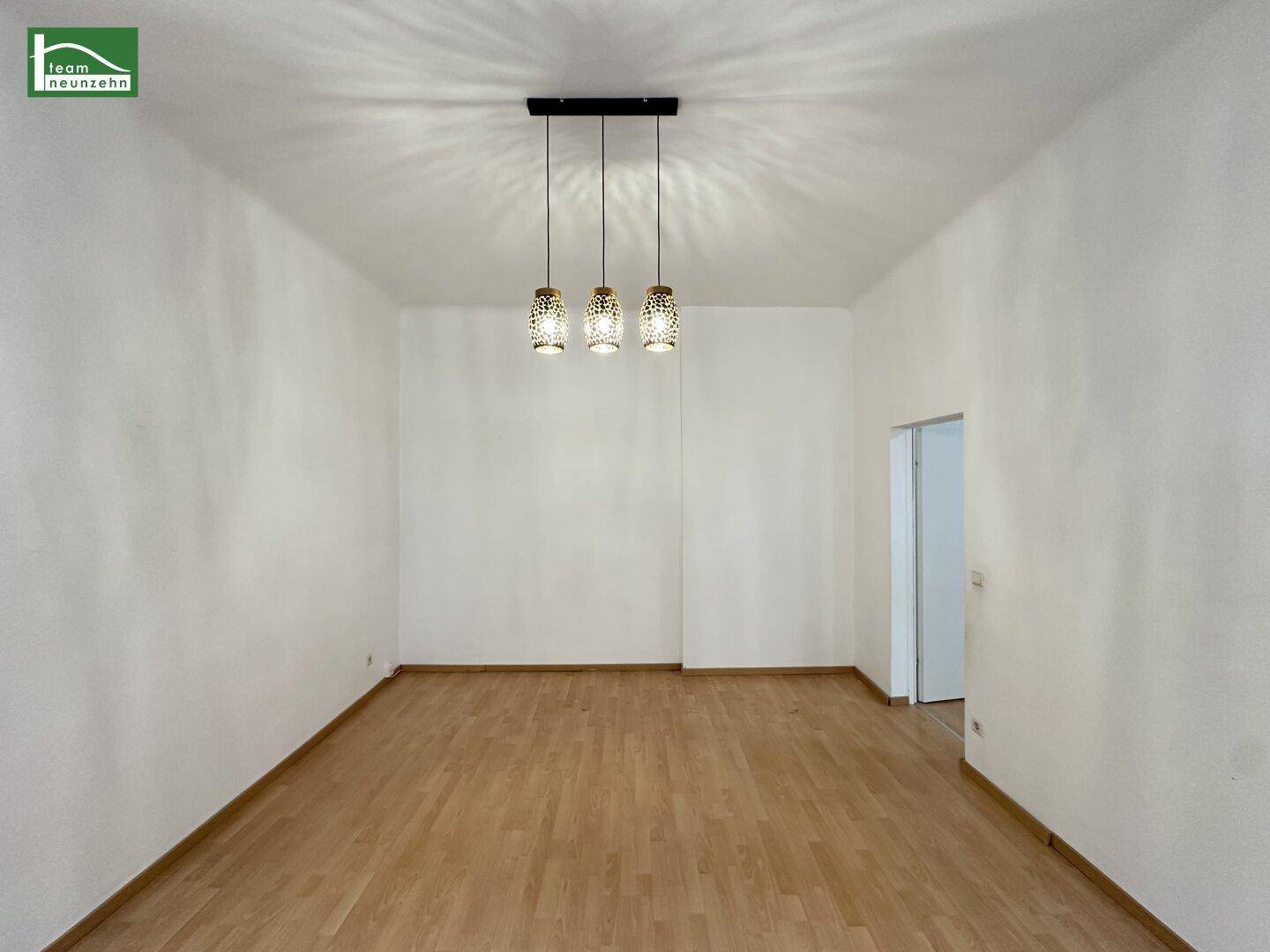 Geräumiger, heller Raum mit Holzparkett und Zugang zu weiteren Zimmern.