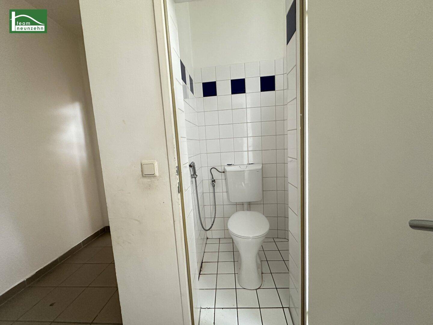 Kleines WC mit Toilette und weißen Fliesen, akzentuiert durch blaue Details.