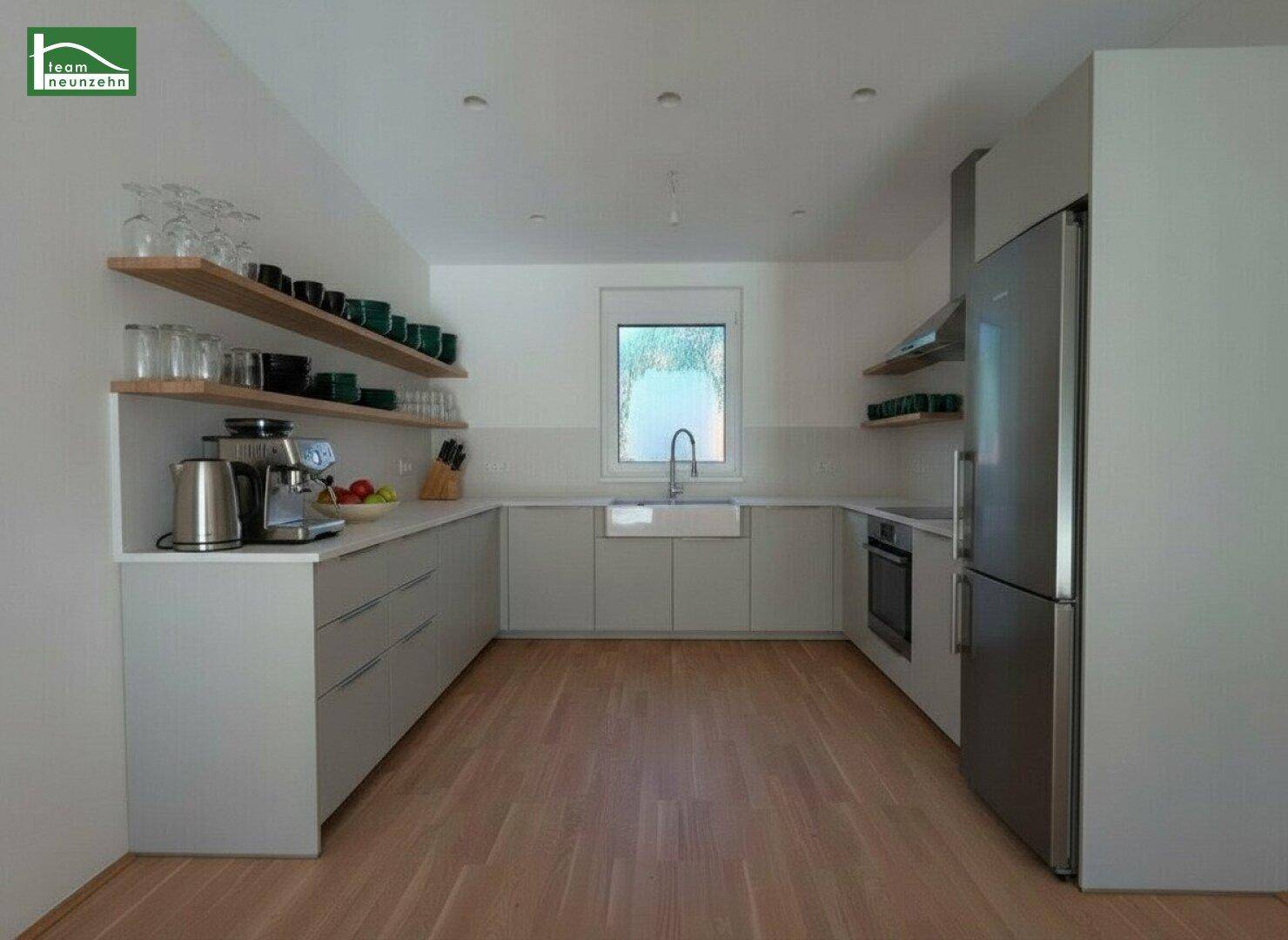 Moderne Küche mit hellgrauen Schränken, Holzboden und Fenster über der Spüle.