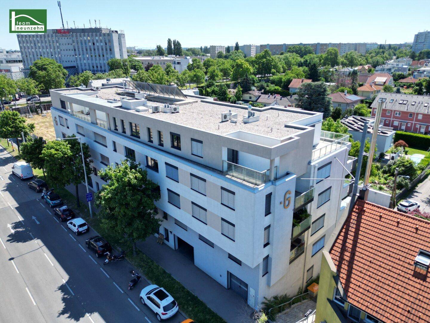 Modernes Wohngebäude mit weißer Fassade, Flachdach und Balkonen, umgeben von Bäumen und einer ruhigen Wohnstraße.