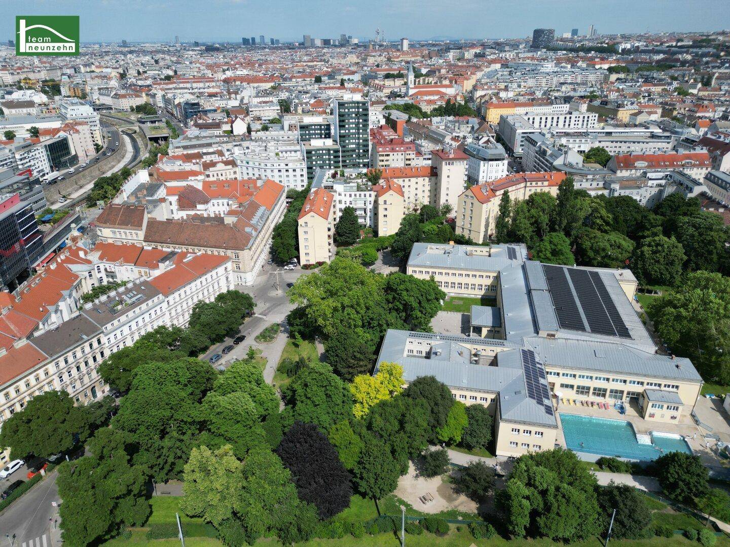 Luftaufnahme eines Stadtteils mit Parkanlagen, Gebäuden und einem Schwimmbad.