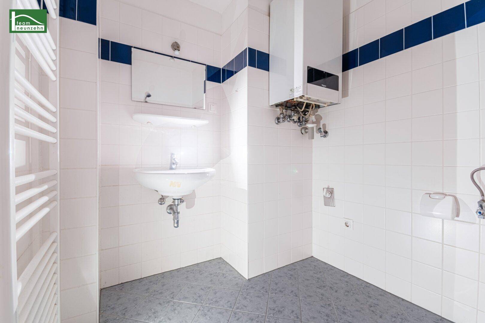 Badezimmer mit Waschbecken, Spiegel und Gastherme, umgeben von weißen Fliesen und blauen Akzenten.