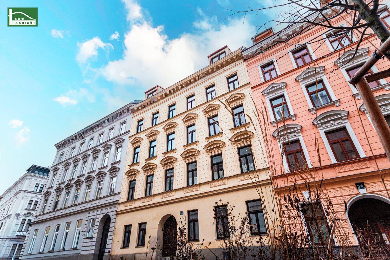 Historische Fassade eines Mehrfamilienhauses mit vielen Fenstern unter blauem Himmel.