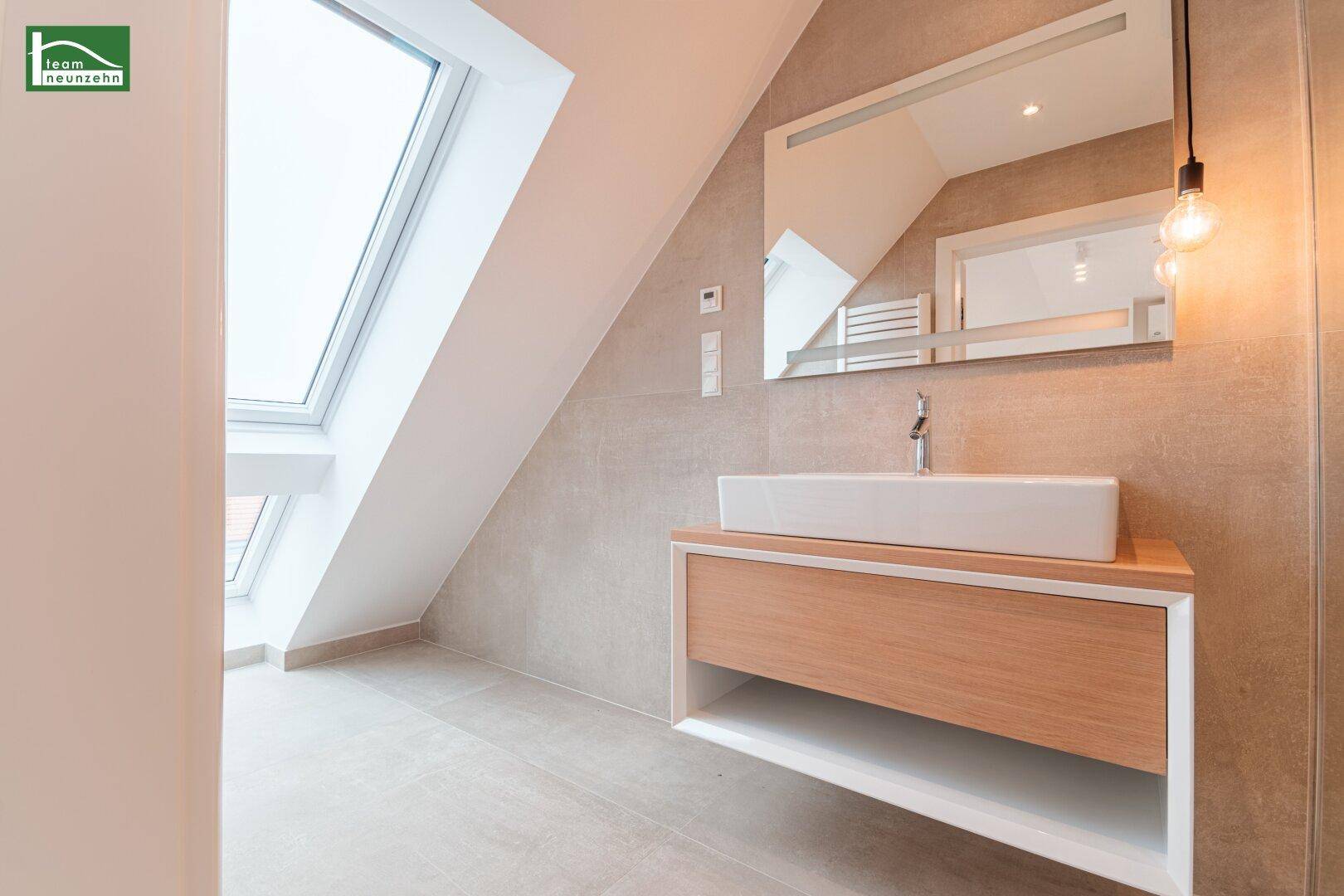 Helles Badezimmer mit Waschtisch, großem Spiegel und Dachfenster für natürliches Licht.