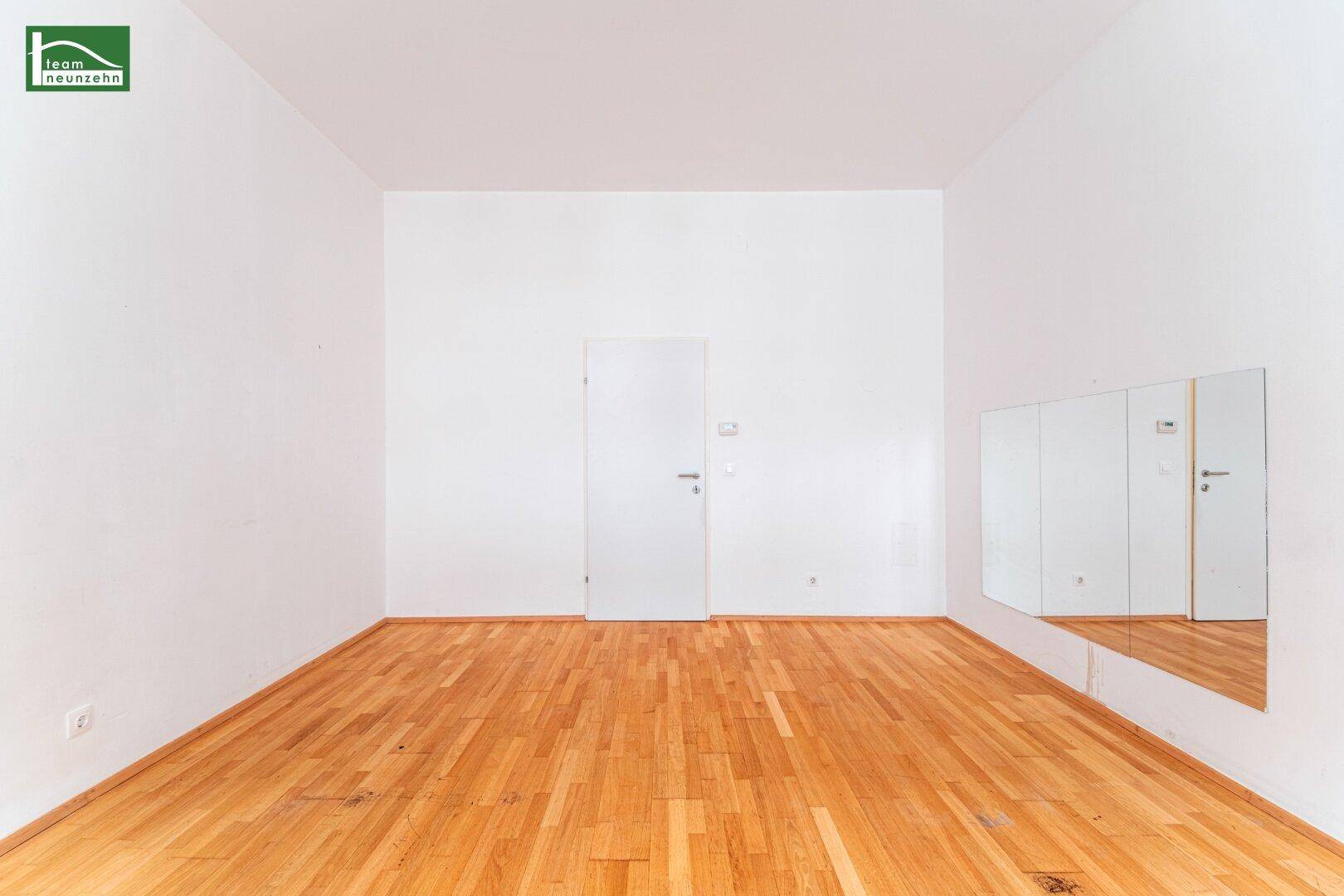 Geräumiger, leerer Raum mit Parkettboden und einer Wand mit Spiegelflächen.