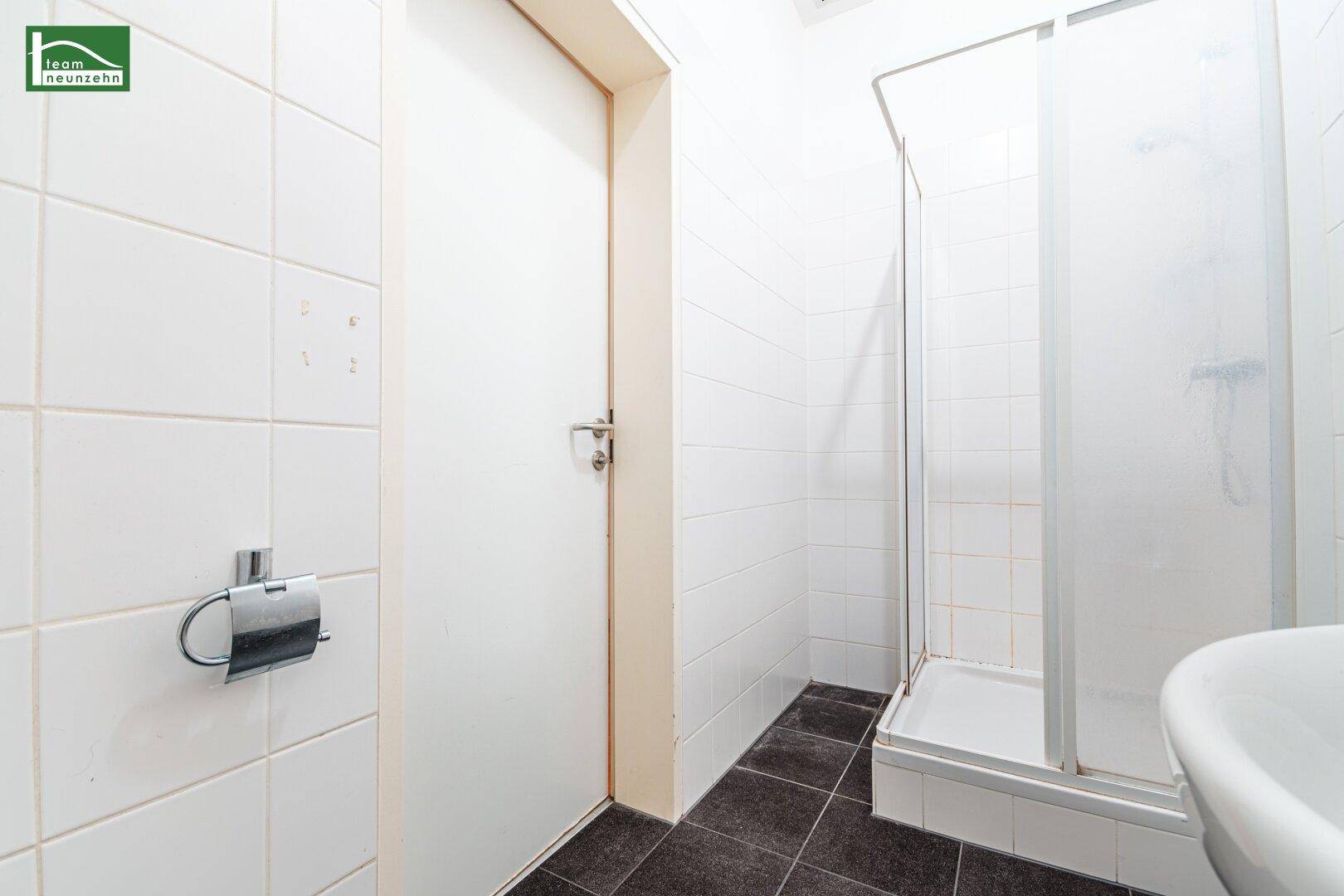 Badezimmer mit Duschkabine, Waschbecken und weißen Fliesen an den Wänden.
