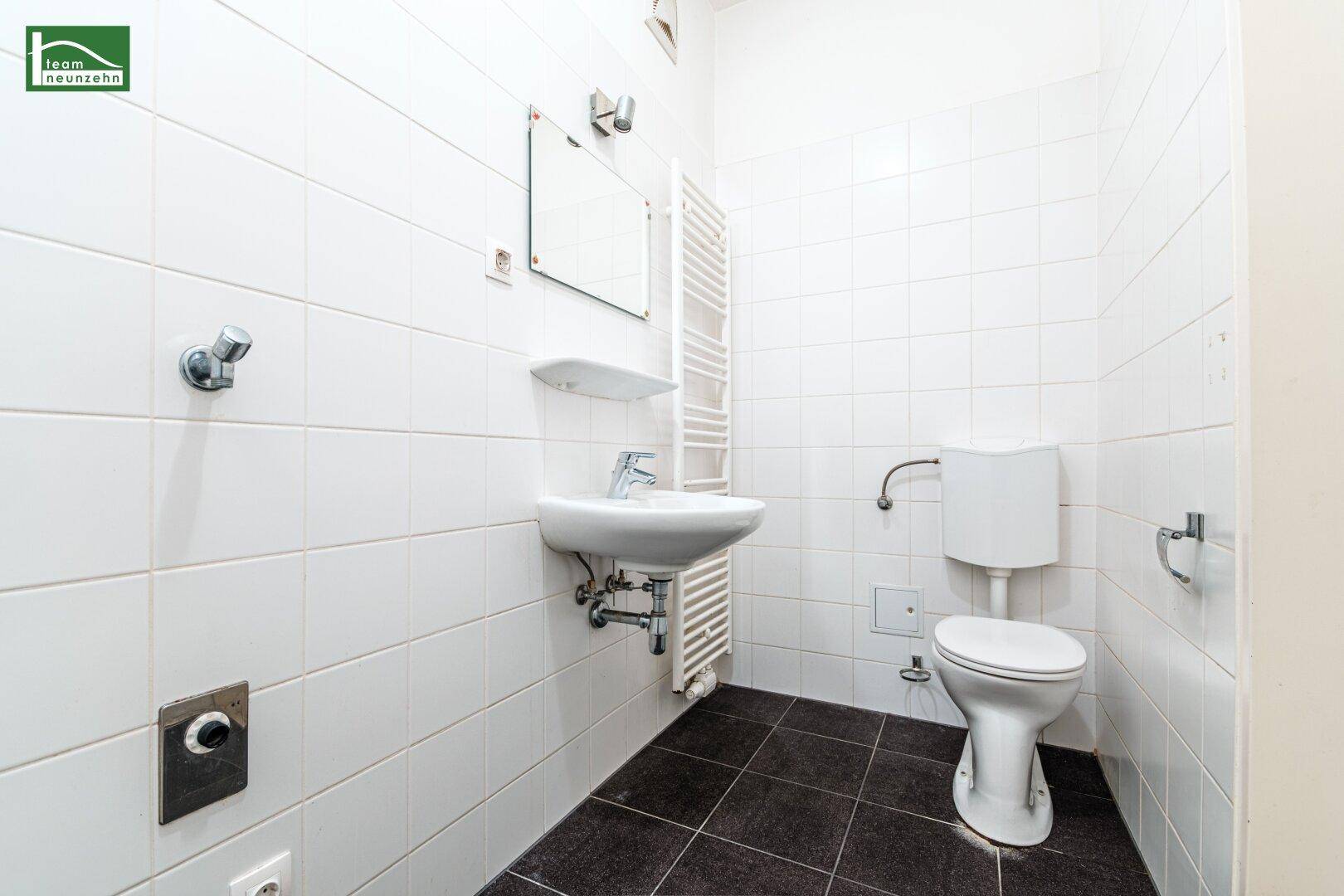 Modernes Badezimmer mit weißen Fliesen, dunklem Boden und wandmontiertem WC und Waschbecken.