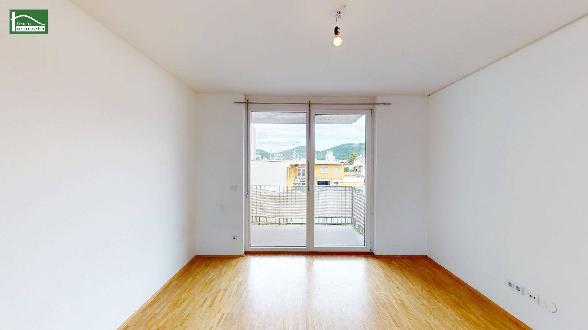 Helles, leeres Wohnzimmer mit Parkettboden und Zugang zu einem Balkon, ideal für individuelle Gestaltung.