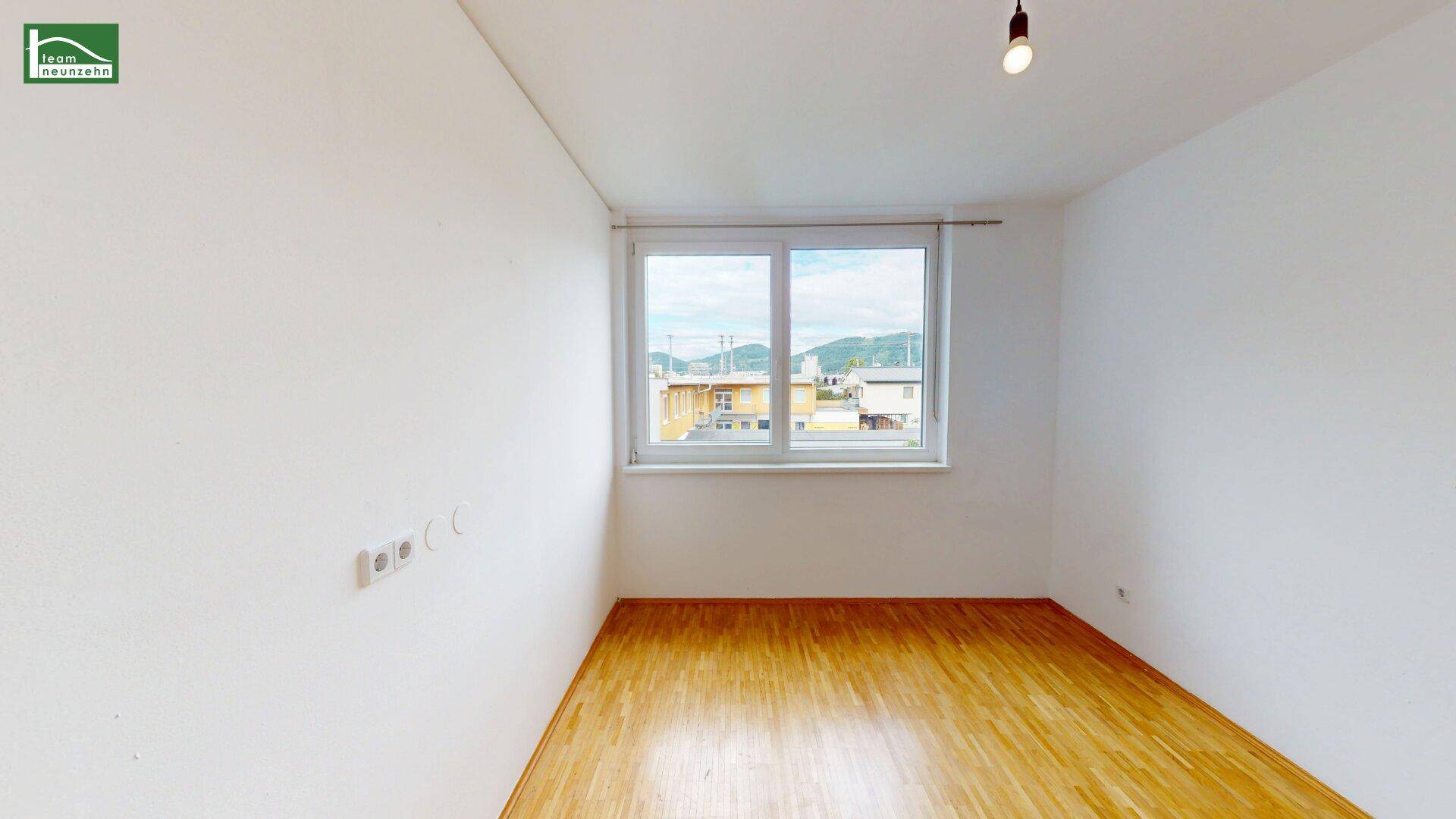 Leeres Schlafzimmer mit Parkettboden und großem Fenster, bietet viel Tageslicht und Ausblick.