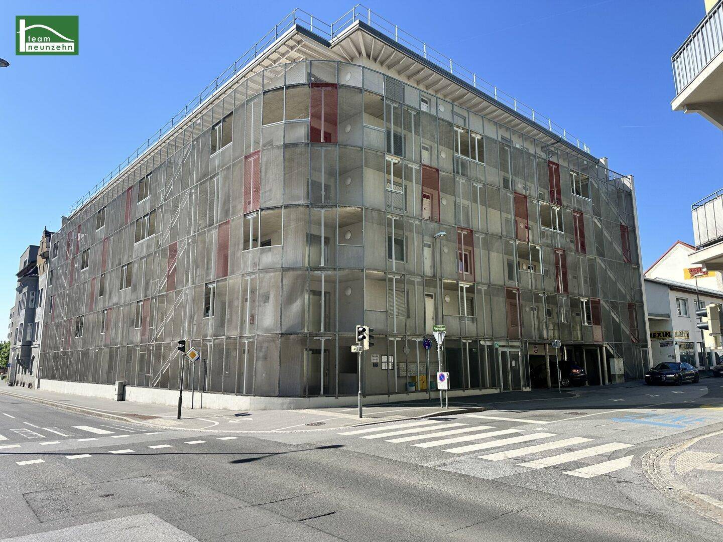 Moderne Gebäudefassade mit Glas- und Metallstrukturen an einer städtischen Kreuzung.
