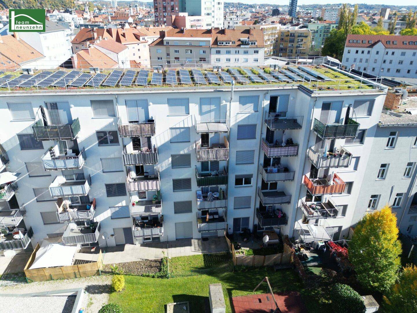 Luftaufnahme eines Wohngebäudes mit Balkonen, Solaranlagen auf dem Dach und einem grünen Innenhof.