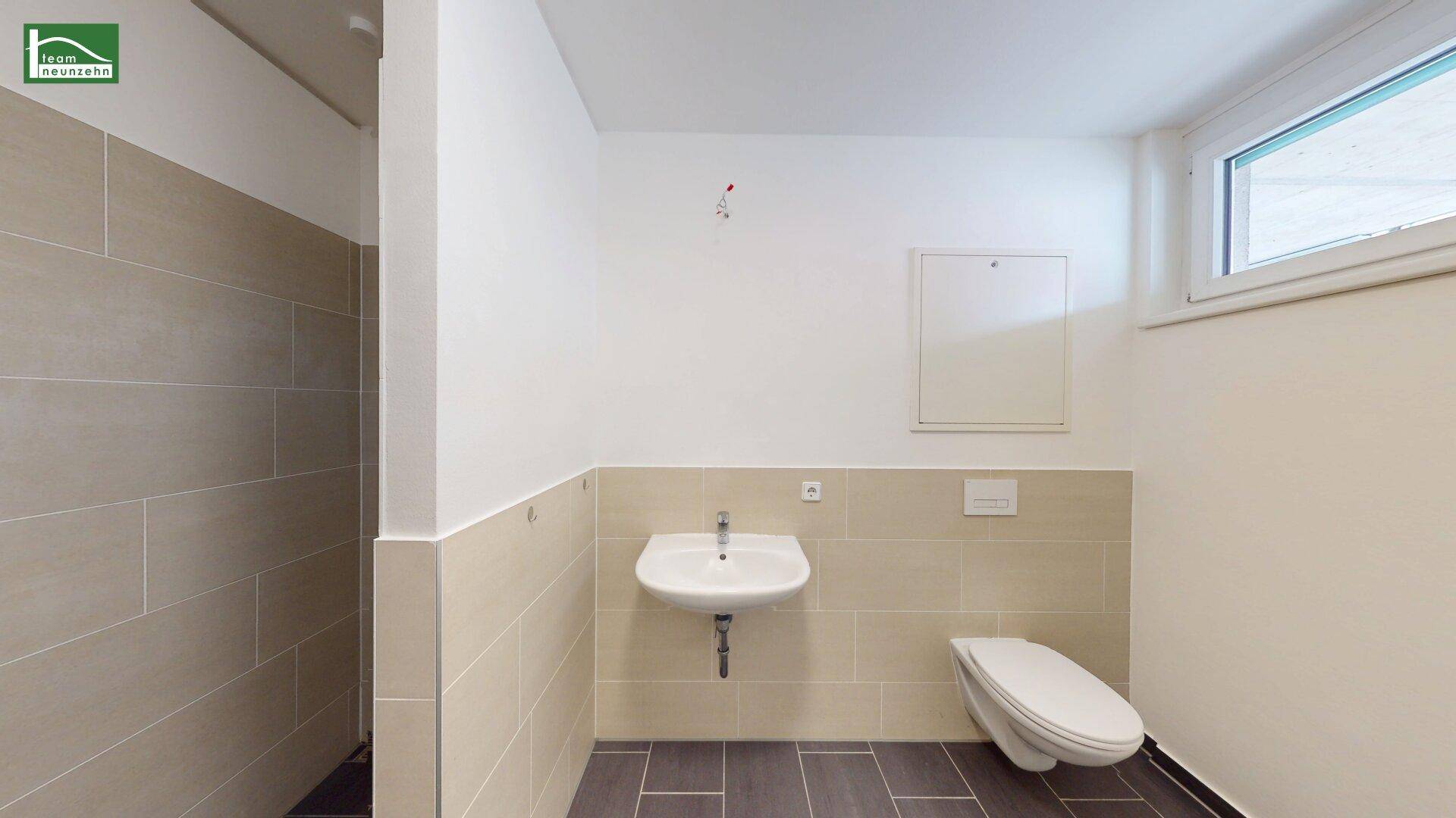 Modernes Badezimmer mit Fliesenboden, wandhängendem WC, Waschbecken und Duschbereich.