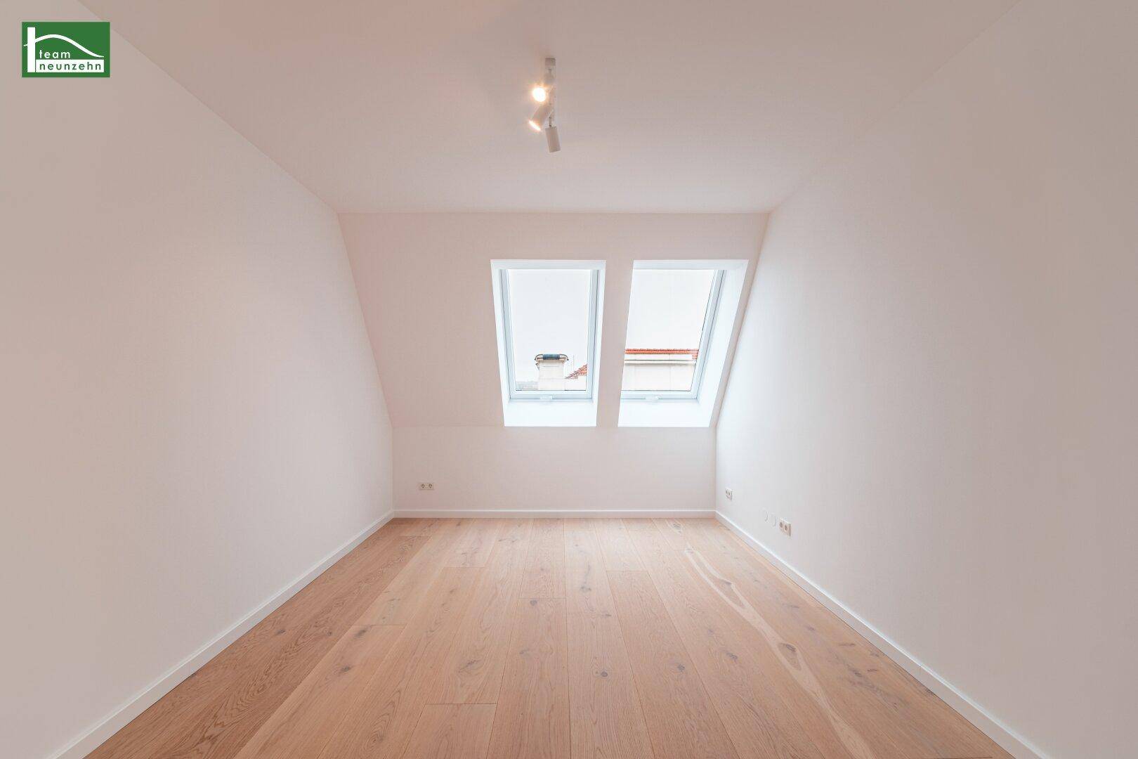 Lichtdurchfluteter Raum im Dachgeschoss mit Holzboden und zwei großen Dachfenstern.