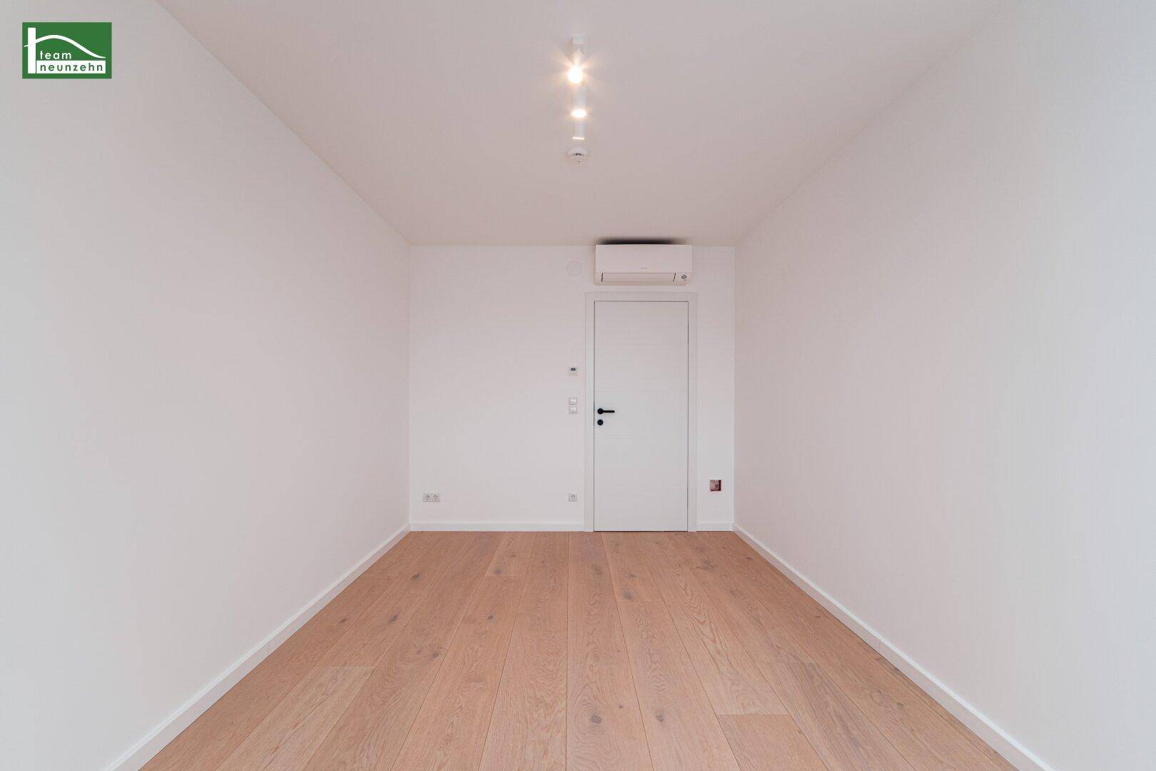 Modernes Zimmer mit Holzboden, Klimaanlage und weiß gestrichenen Wänden.