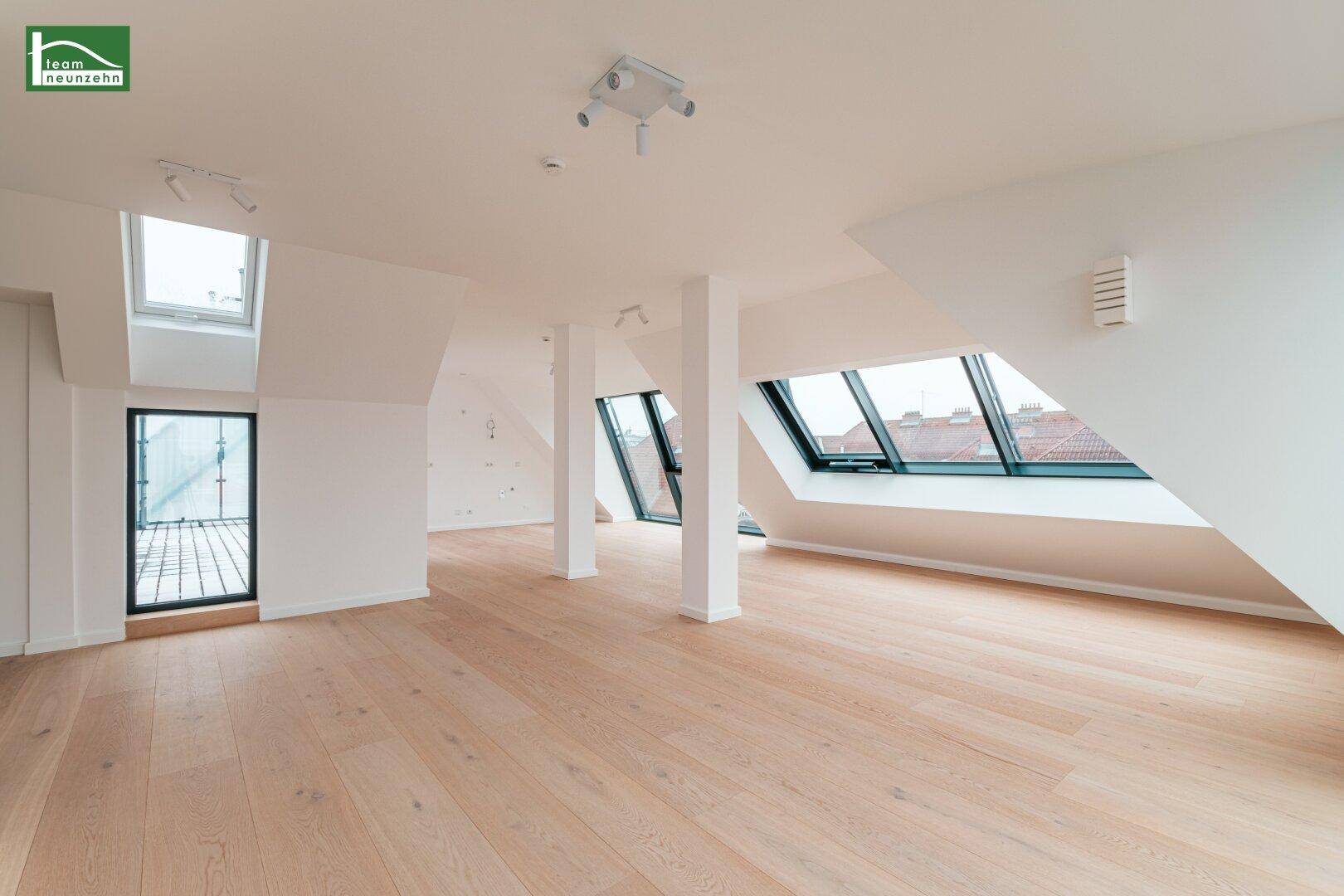 Heller und weitläufiger Wohnbereich mit Holzboden, Säulen und verschiedenen Fensterformen.