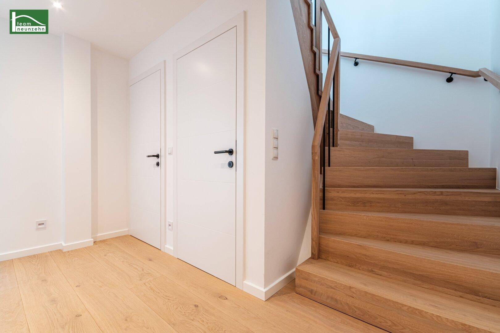 Heller Flurbereich mit Holztreppe und modernen weißen Türen.