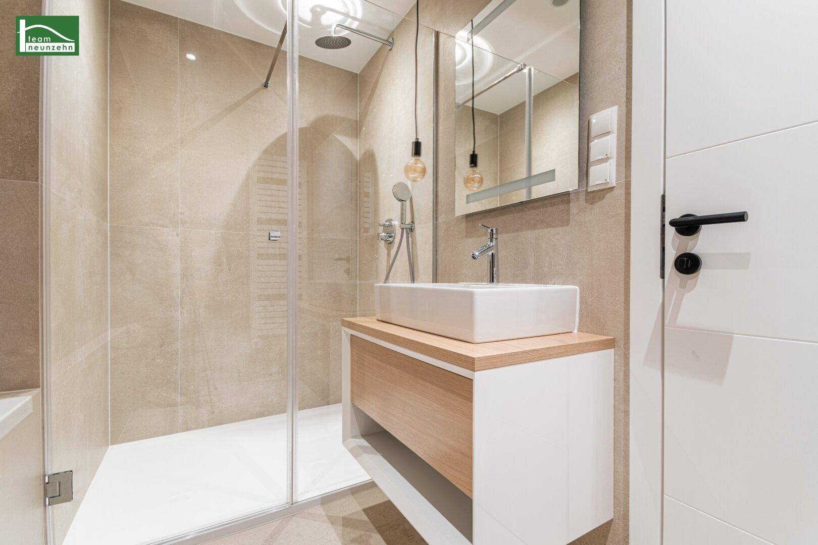 Zeitgemäßes Badezimmer mit großer Dusche, modernem Waschbecken und beheiztem Handtuchhalter.