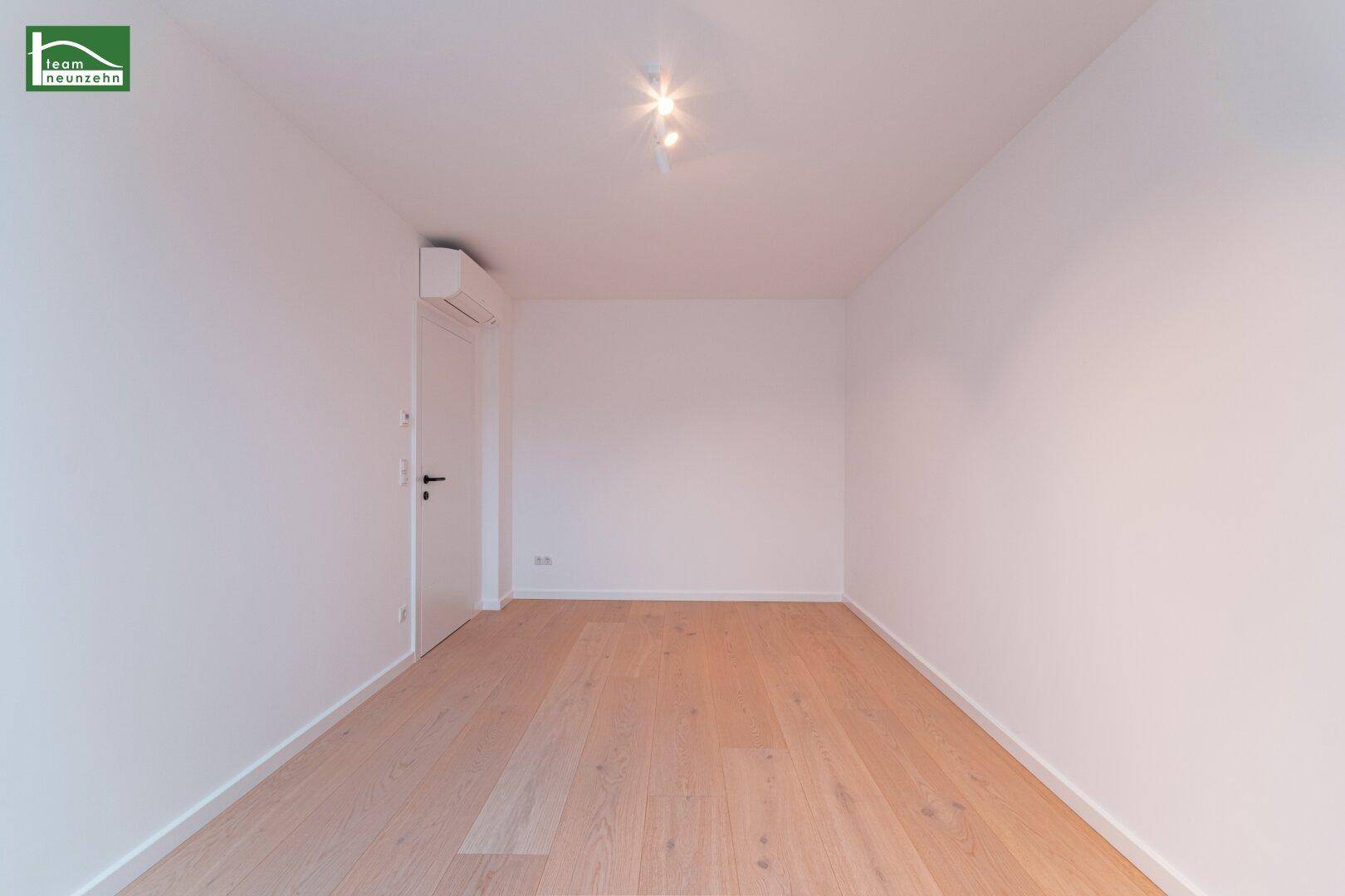Leeres Zimmer mit hellem Holzboden, weißen Wänden und Klimaanlage, bereit zur individuellen Gestaltung.