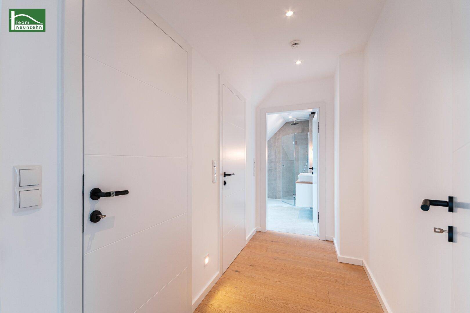 Heller Flur mit Holzboden und modernen weißen Türen, der zu weiteren Zimmern und einem Badezimmer führt.