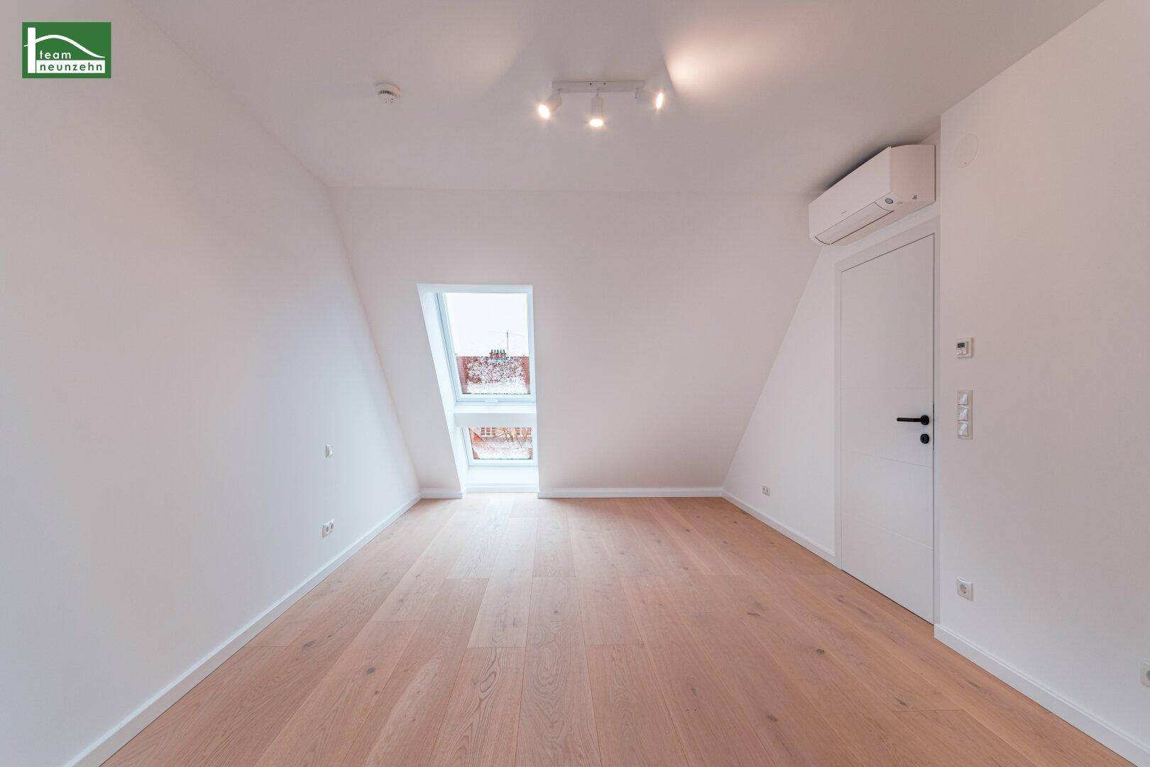 Geräumiges Dachzimmer mit einem Dachfenster, Klimaanlage und hellem Holzfußboden.