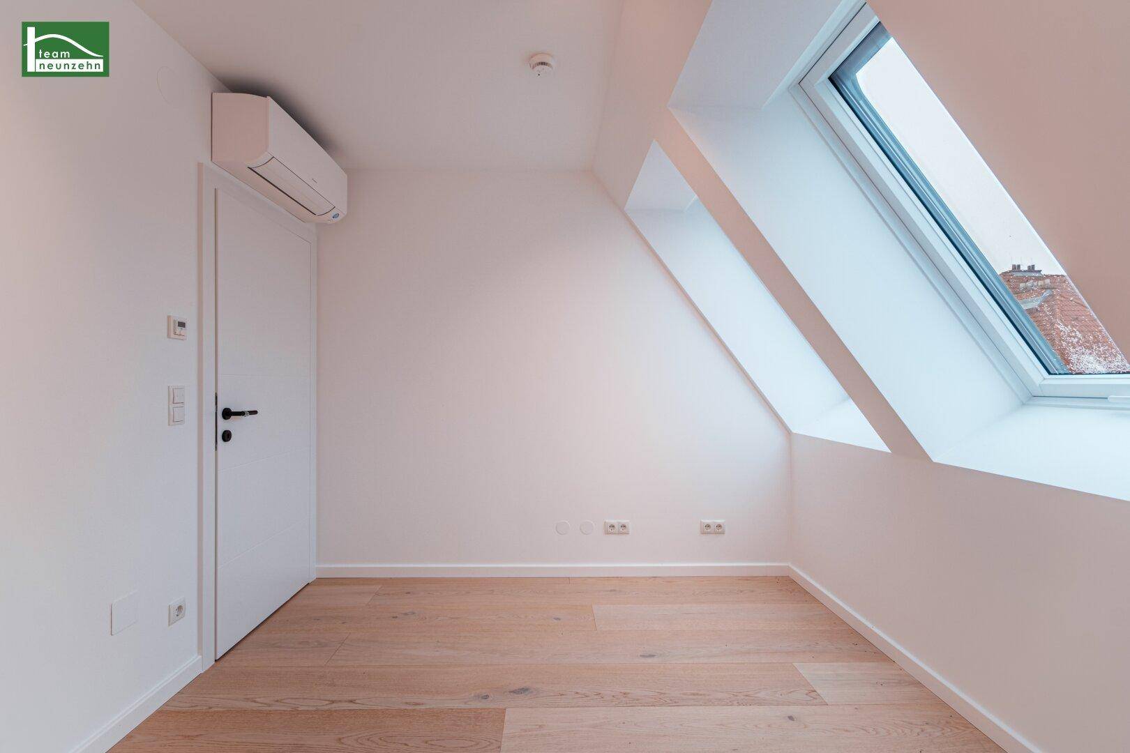 Helles Dachzimmer mit einem großen Dachfenster, Klimaanlage und Holzfußboden.