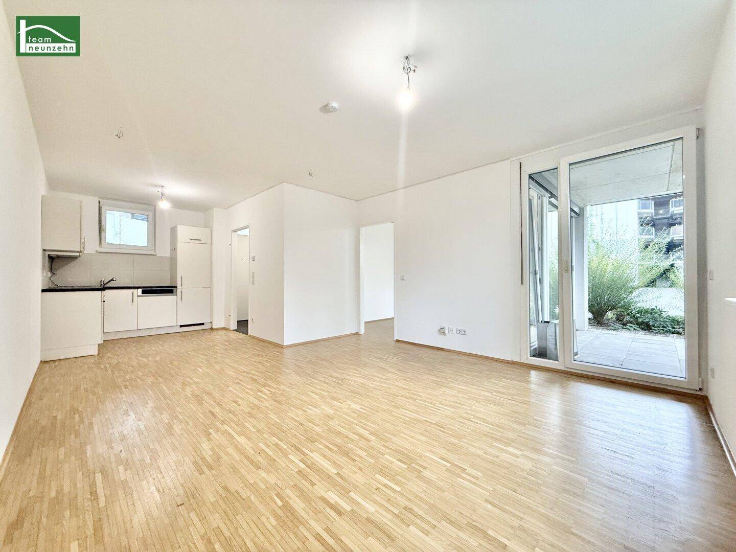 Geräumiger Wohnbereich mit integrierter Küchenzeile, Holzboden und Terrassenzugang.