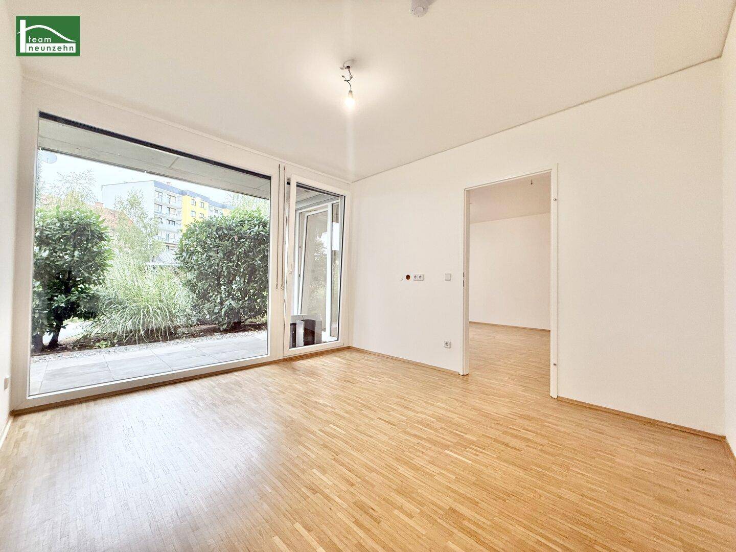 Heller Raum mit Parkettboden und großem Schiebetürzugang zu einem begrünten Außenbereich.