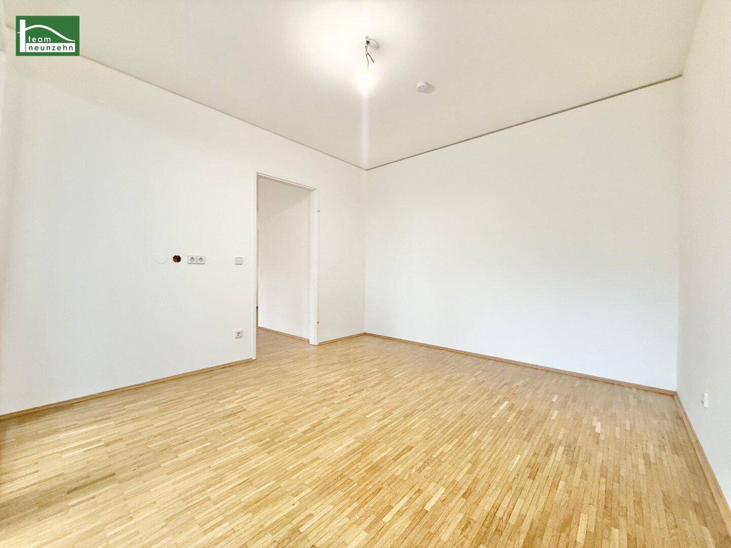 Leerer Raum mit hellem Parkettboden und weißen Wänden, bereit zur individuellen Gestaltung.