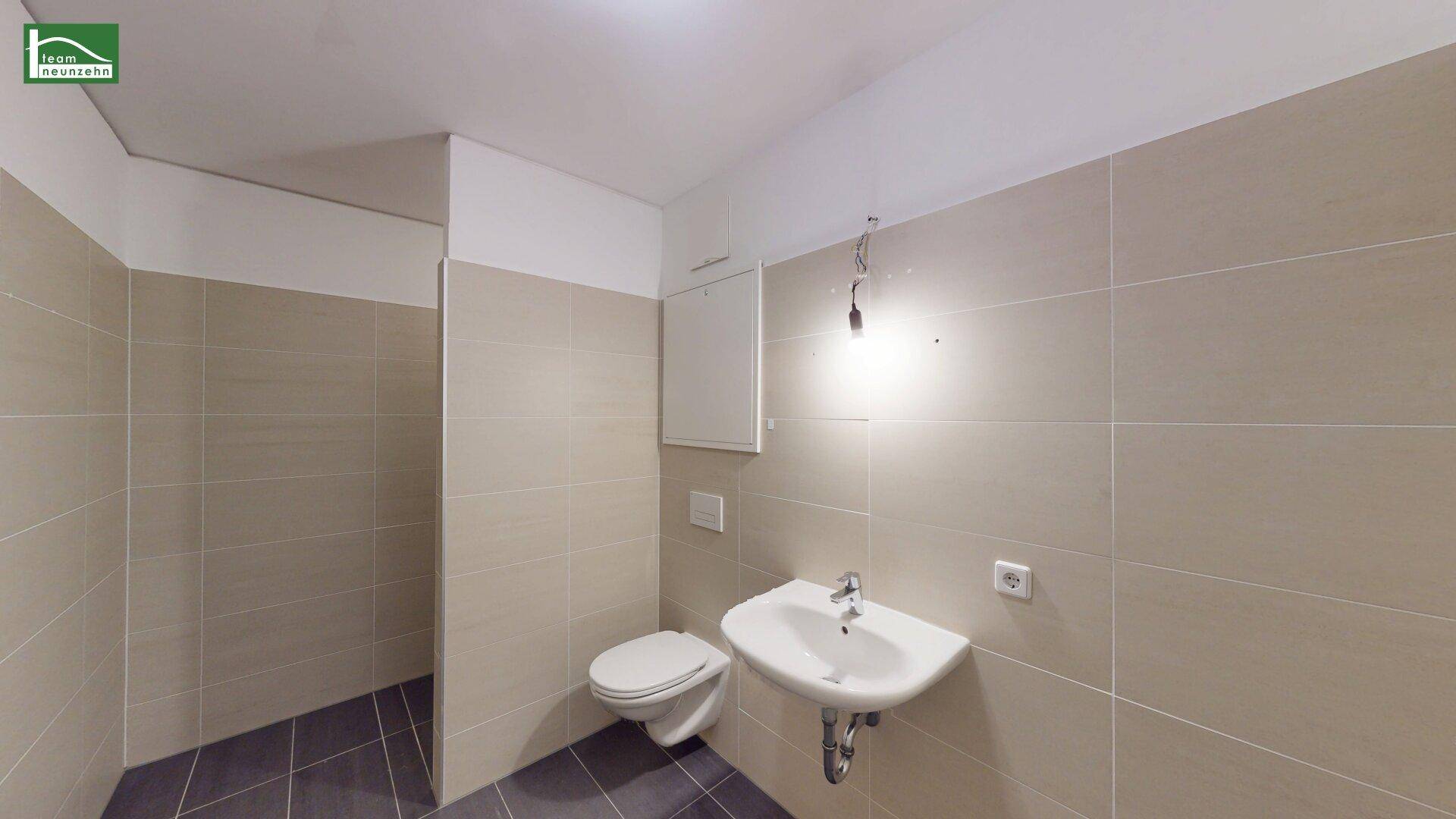 Modernes Badezimmer mit beigen Wandfliesen, dunklem Boden und wandhängendem WC.