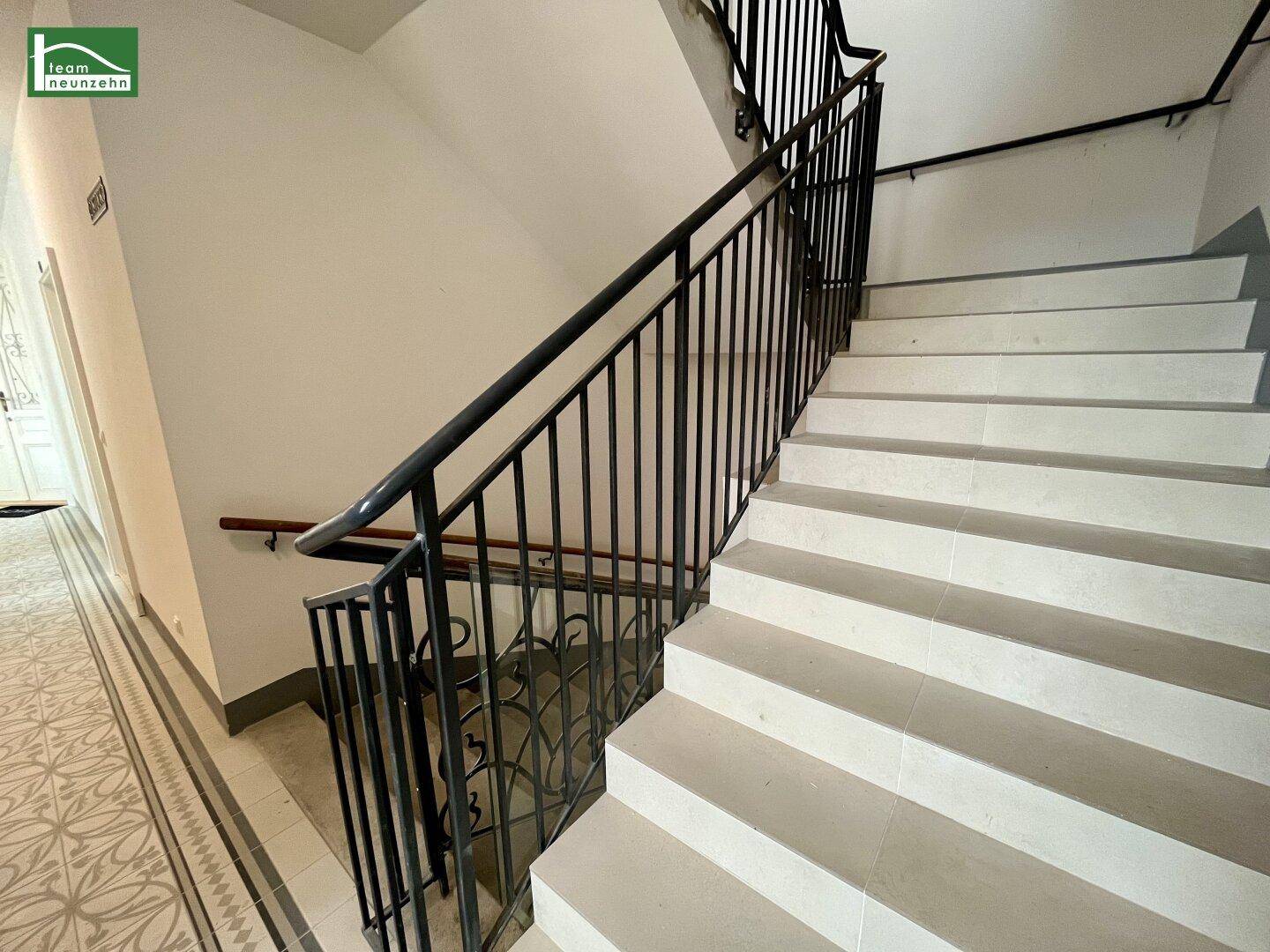 Helles Treppenhaus mit schlichtem Metallgeländer und Holzhandlauf, das zu den oberen Etagen führt.